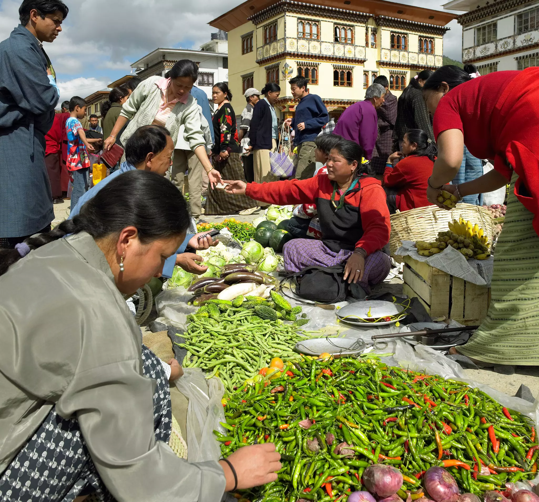 People crowded around green and red chilies and other items at an outdoor food market