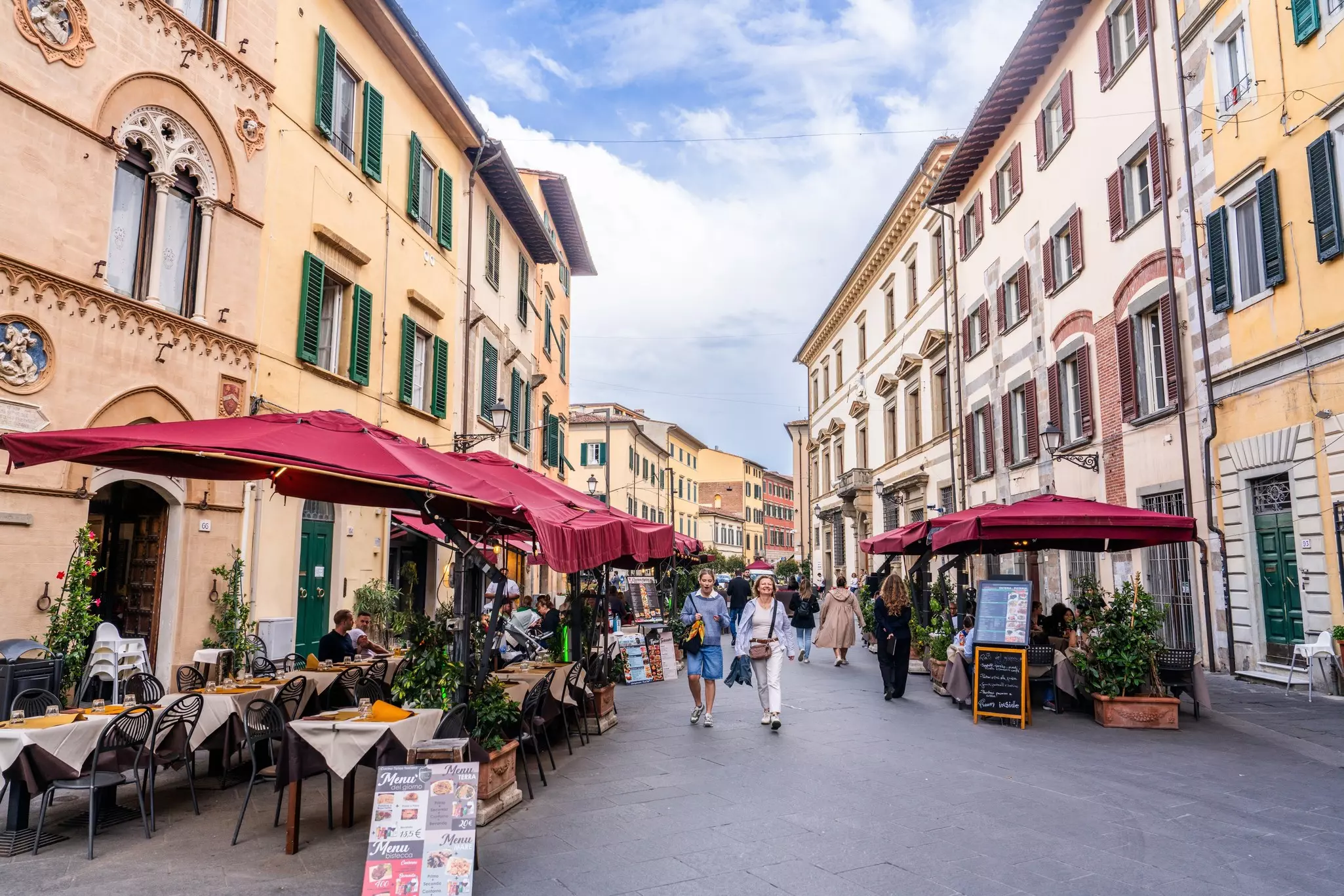 People walking a street lined with restaurants with outdoor terraces.