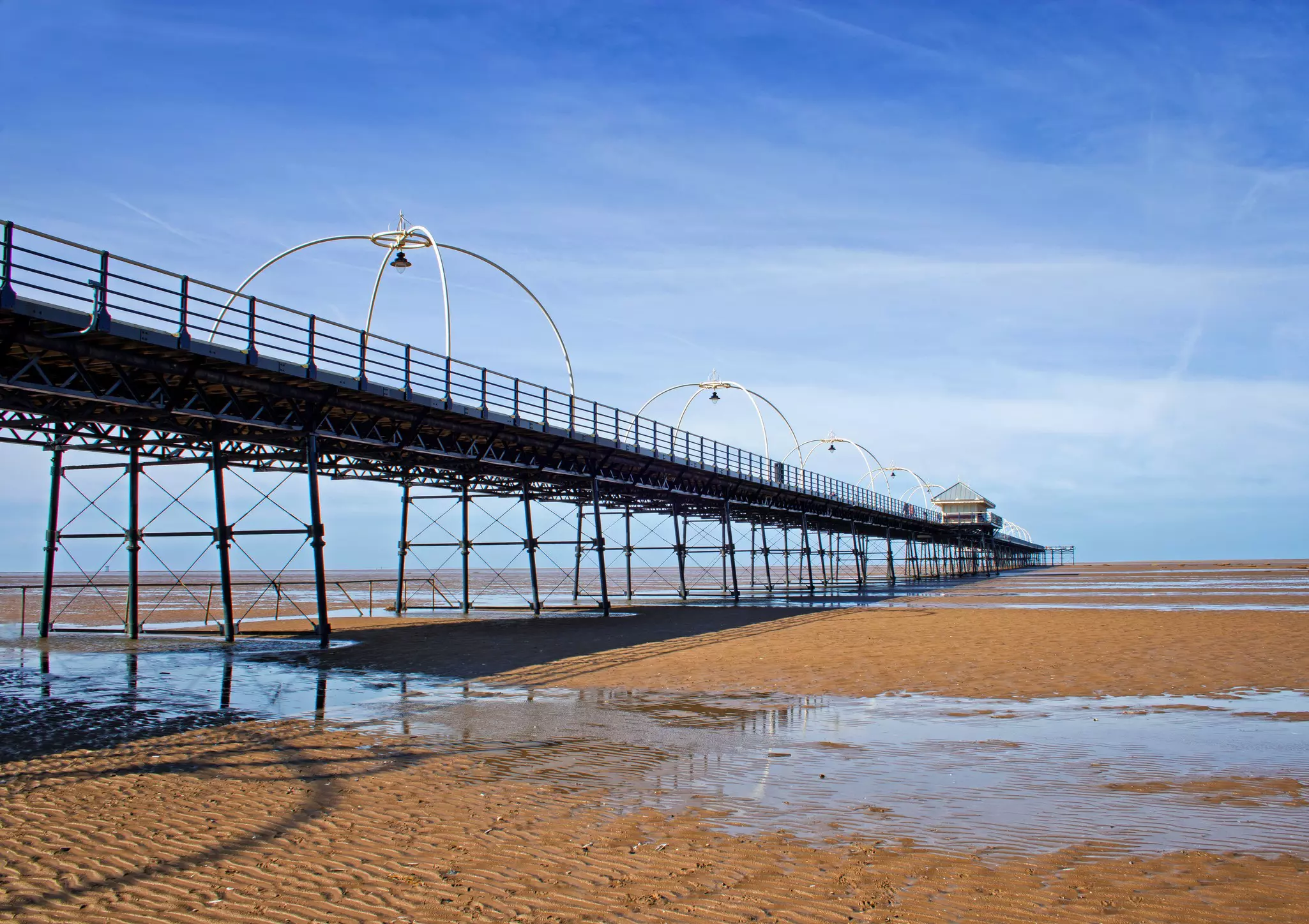 A long pier stretches out over a sandy beach and onwards into the sea.