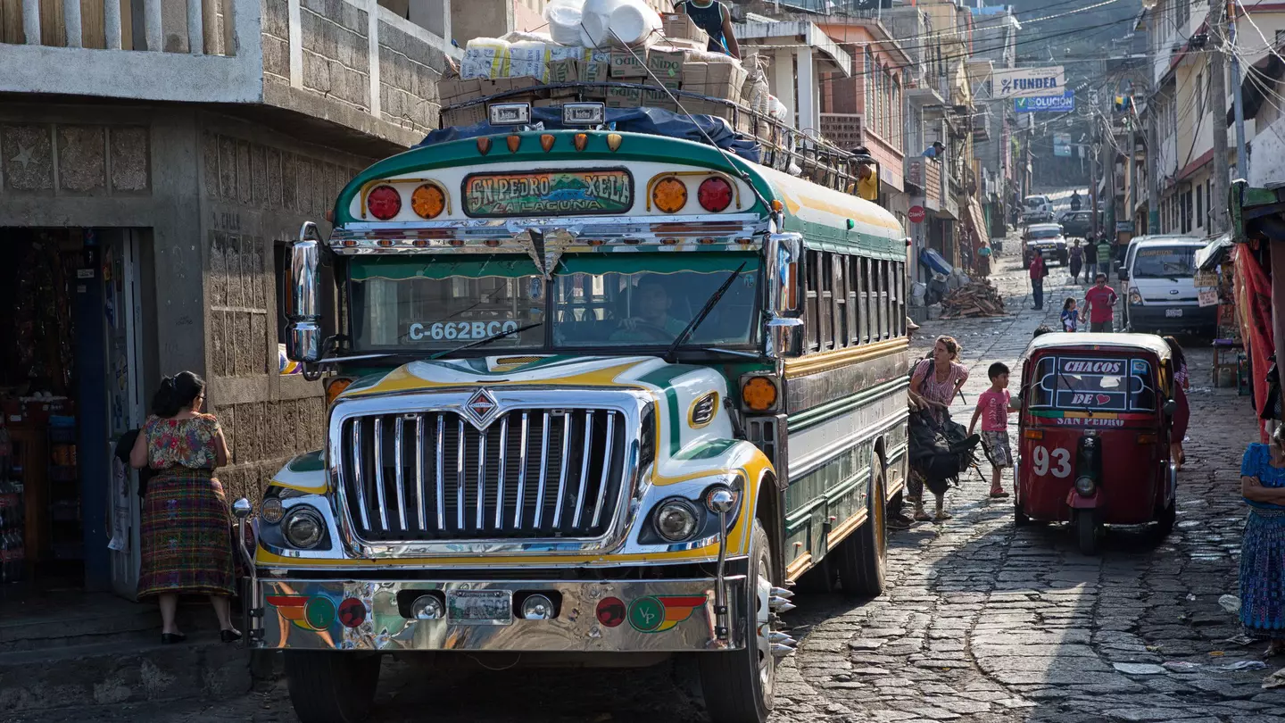 A colorful “chicken bus” (a repainted, purposed school bus) transports riders through the narrow cobblestone streets of San Pedro la Laguna, Guatemala