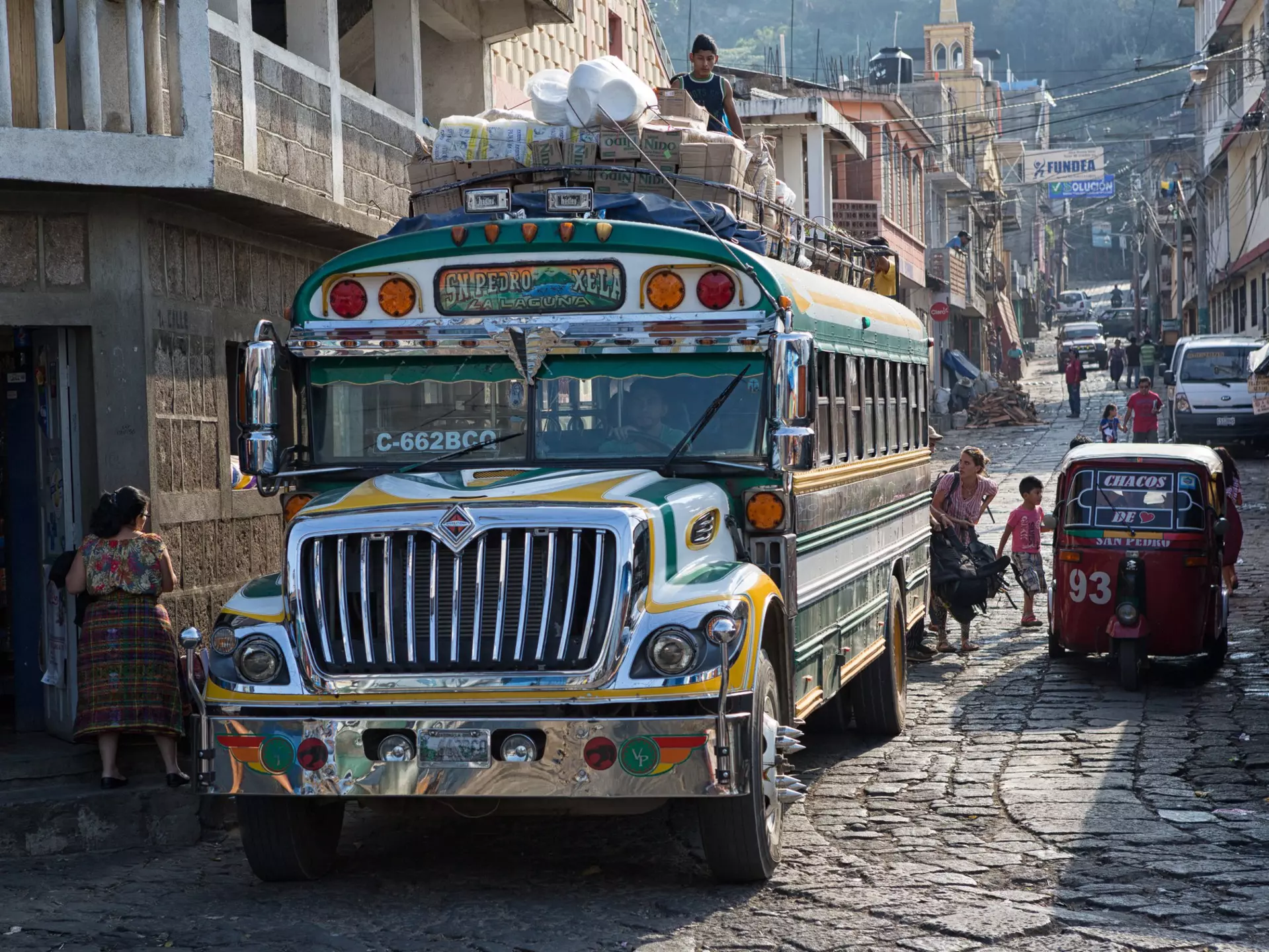 A colorful “chicken bus” (a repainted, purposed school bus) transports riders through the narrow cobblestone streets of San Pedro la Laguna, Guatemala
