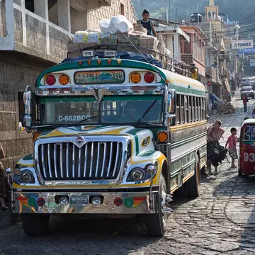 A colorful “chicken bus” (a repainted, purposed school bus) transports riders through the narrow cobblestone streets of San Pedro la Laguna, Guatemala
