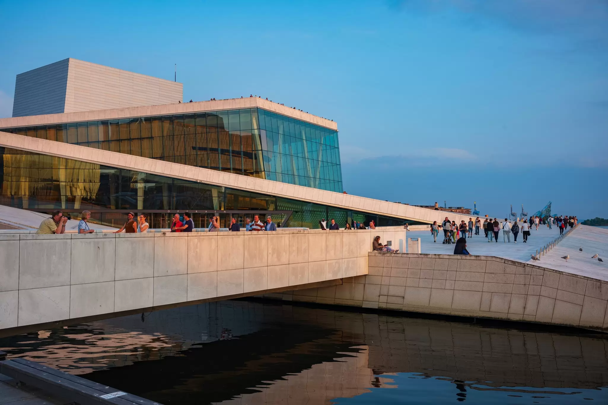 People stand on the roof and on steep paths leading up the sides of a large white building at sunset: Oslo Opera House 