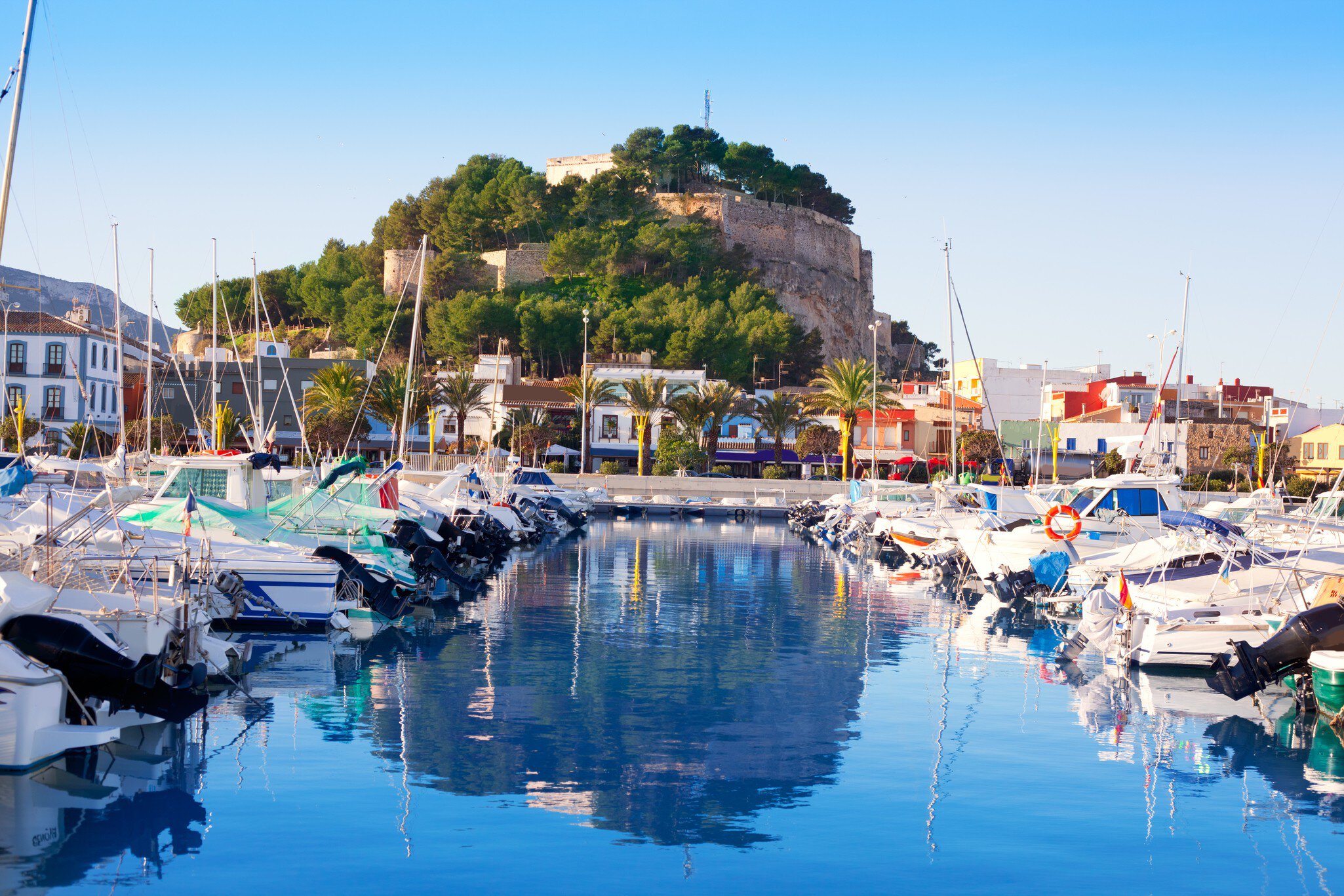 A small harbor packed with sail boats. A hilltop fortress overlooks the water