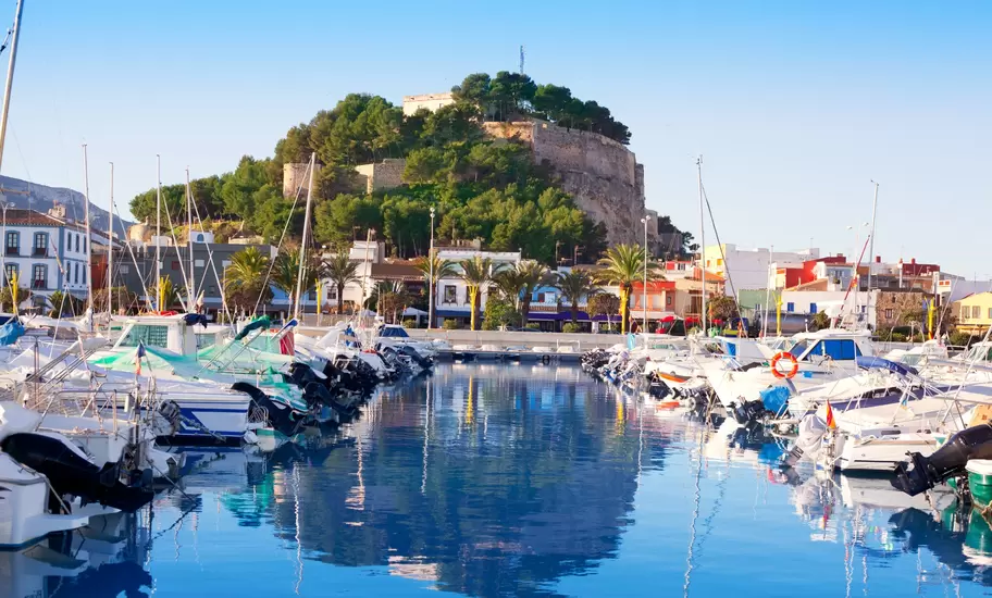 A small harbor packed with sail boats. A hilltop fortress overlooks the water.