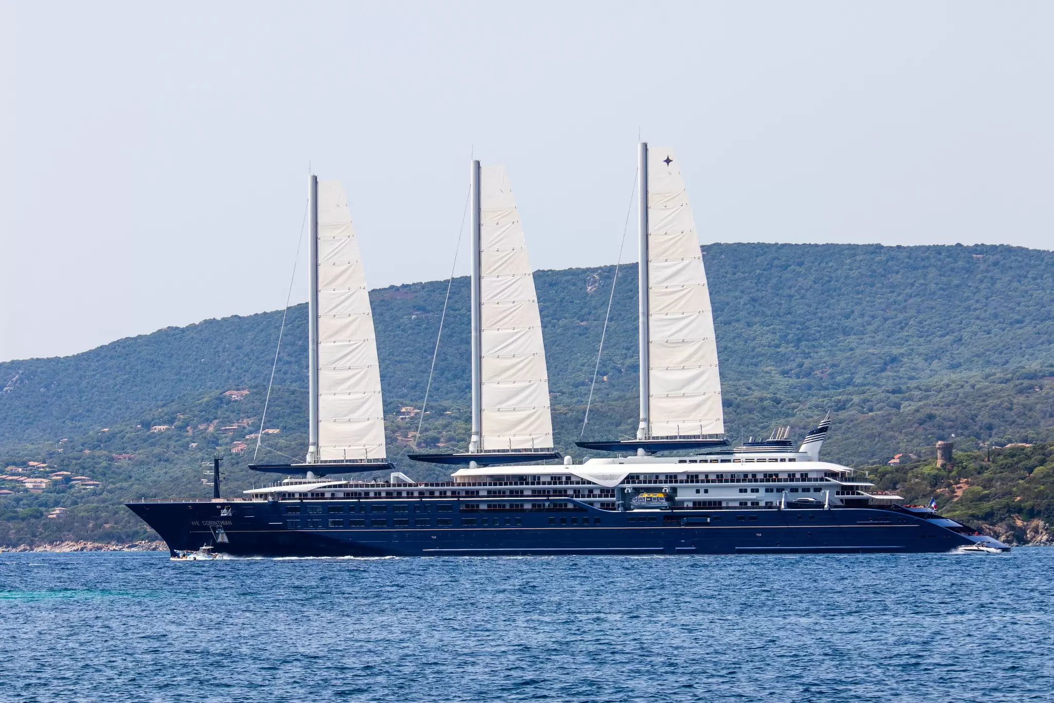 A huge, three-masted sailing yacht is moored in the sea off the coast of Corsica