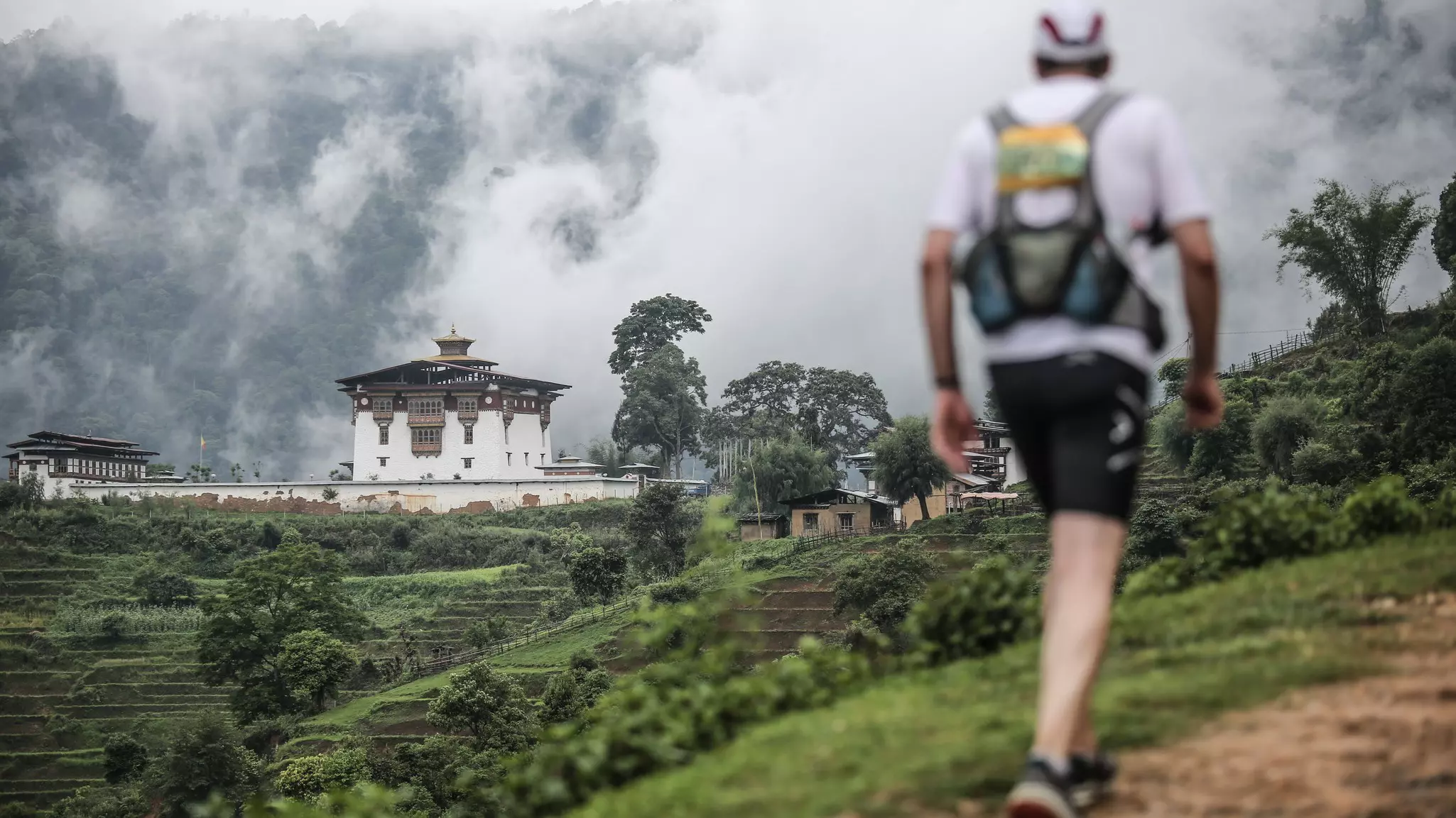 A man with a backpack hikes along a trail by a monastery in Bhutan