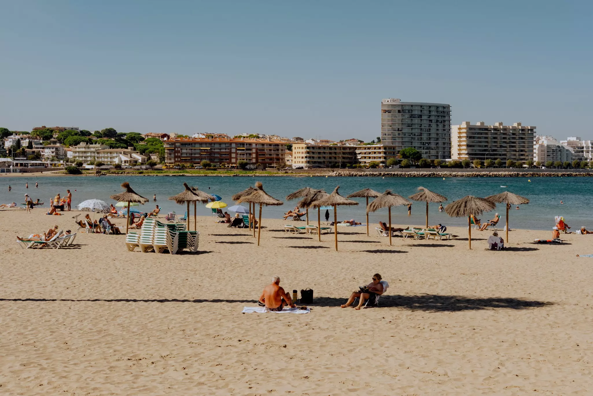 People on a sandy beach with thatched umbrellas.