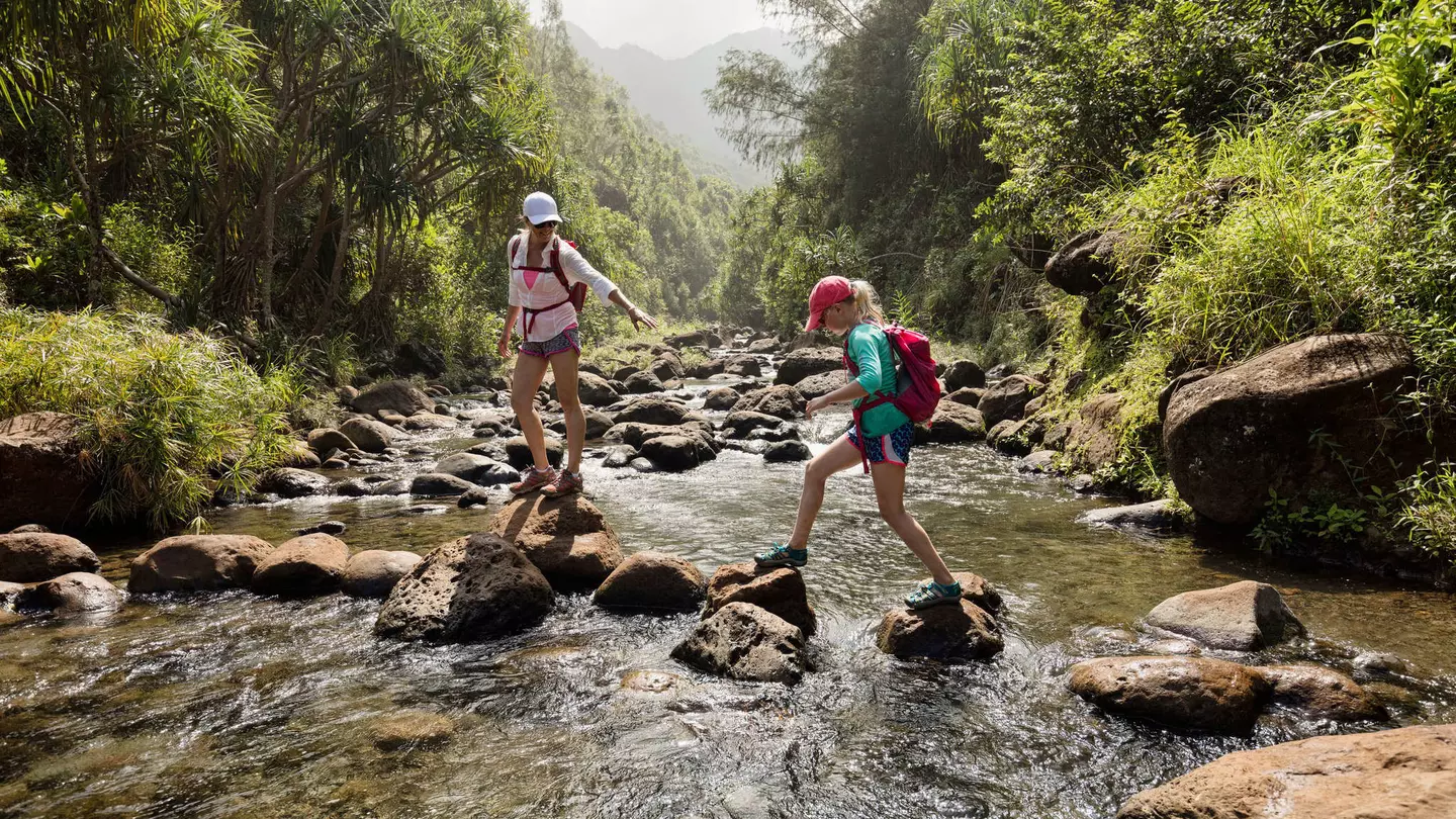 Mother and daughter crossing a creek, Na Pali Coast, Kauai, Hawaii