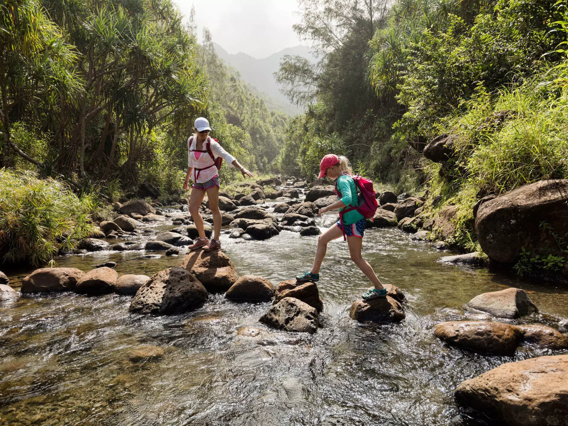 Mother and daughter crossing a creek, Na Pali Coast, Kauai, Hawaii