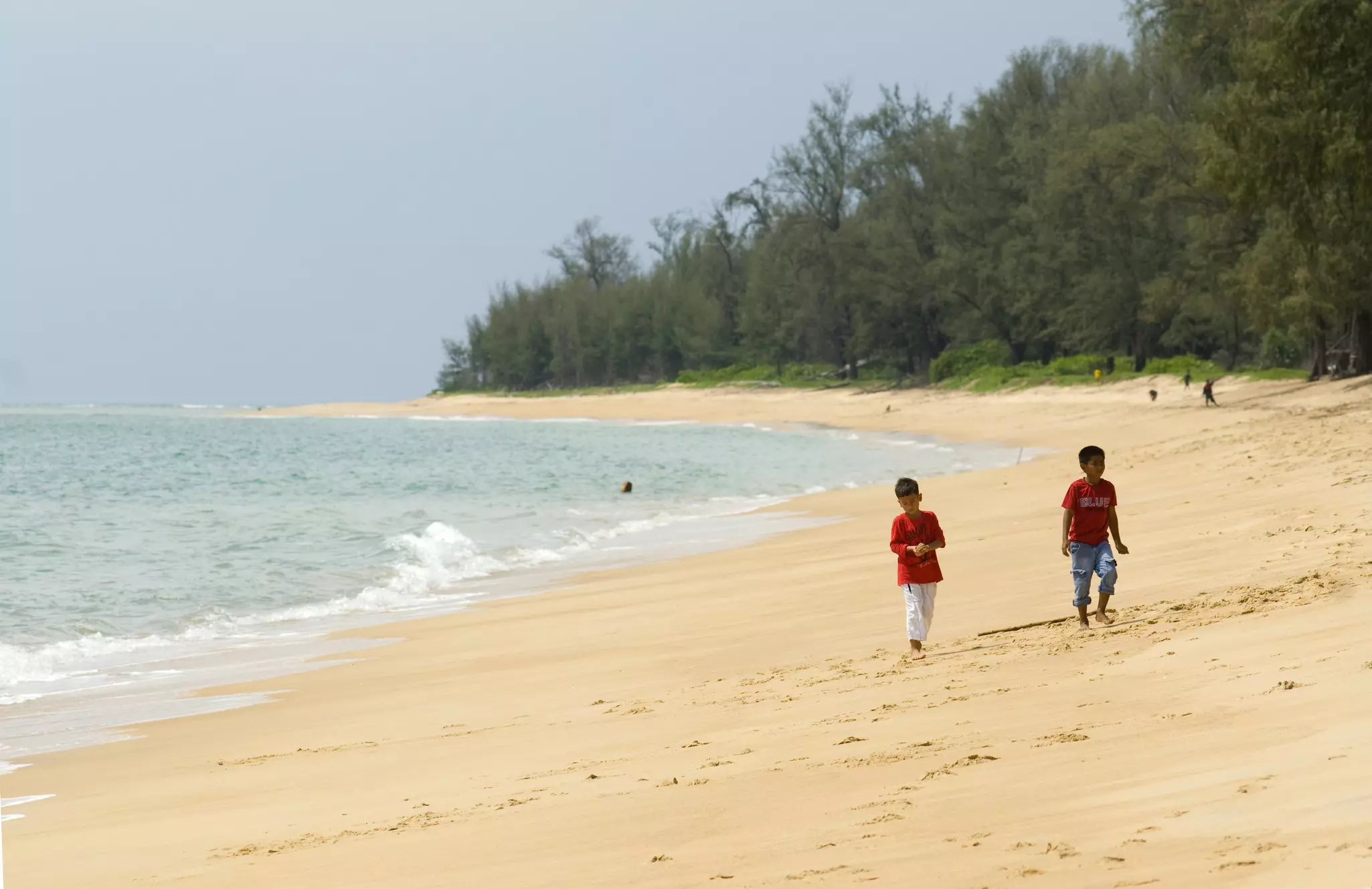 Two children walk on an empty sandy beach.