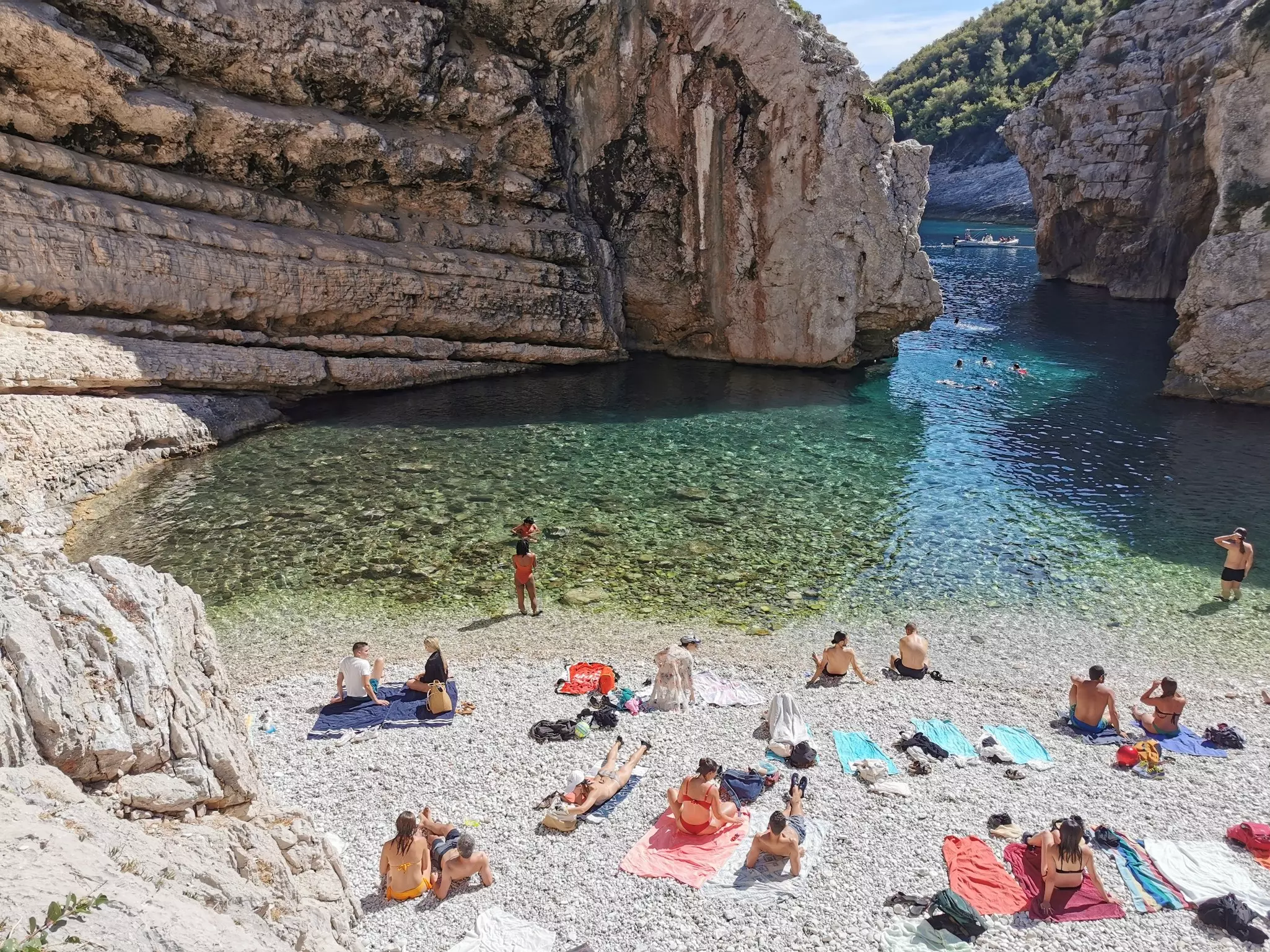 People sunbathe on colorful towels on a rocky shore by a turquoise lagoon