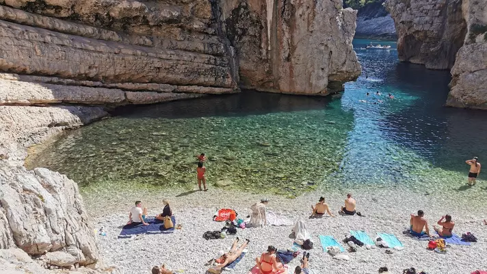 People sunbathe on colorful towels on a rocky shore by a turquoise lagoon