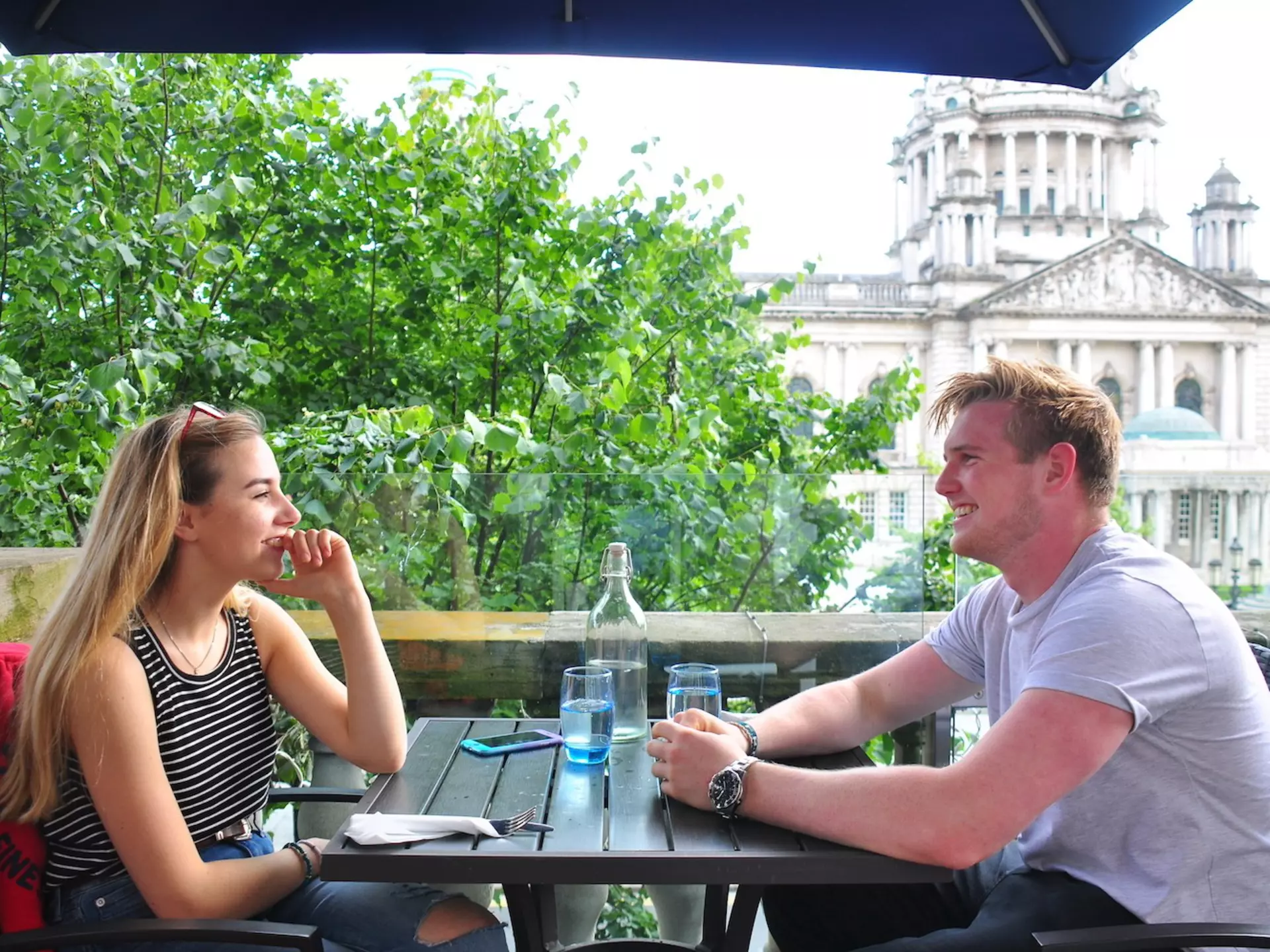 A young couple enjoys a meal at an outdoor table in front of City Hall, Belfast, Northern Ireland, United Kingdom