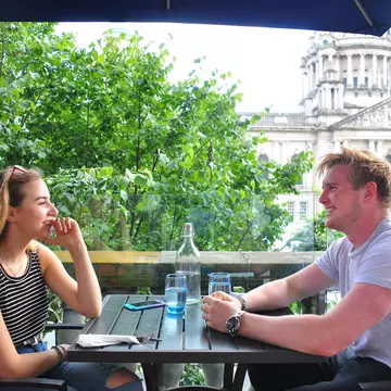 A young couple enjoys a meal at an outdoor table in front of City Hall, Belfast, Northern Ireland, United Kingdom