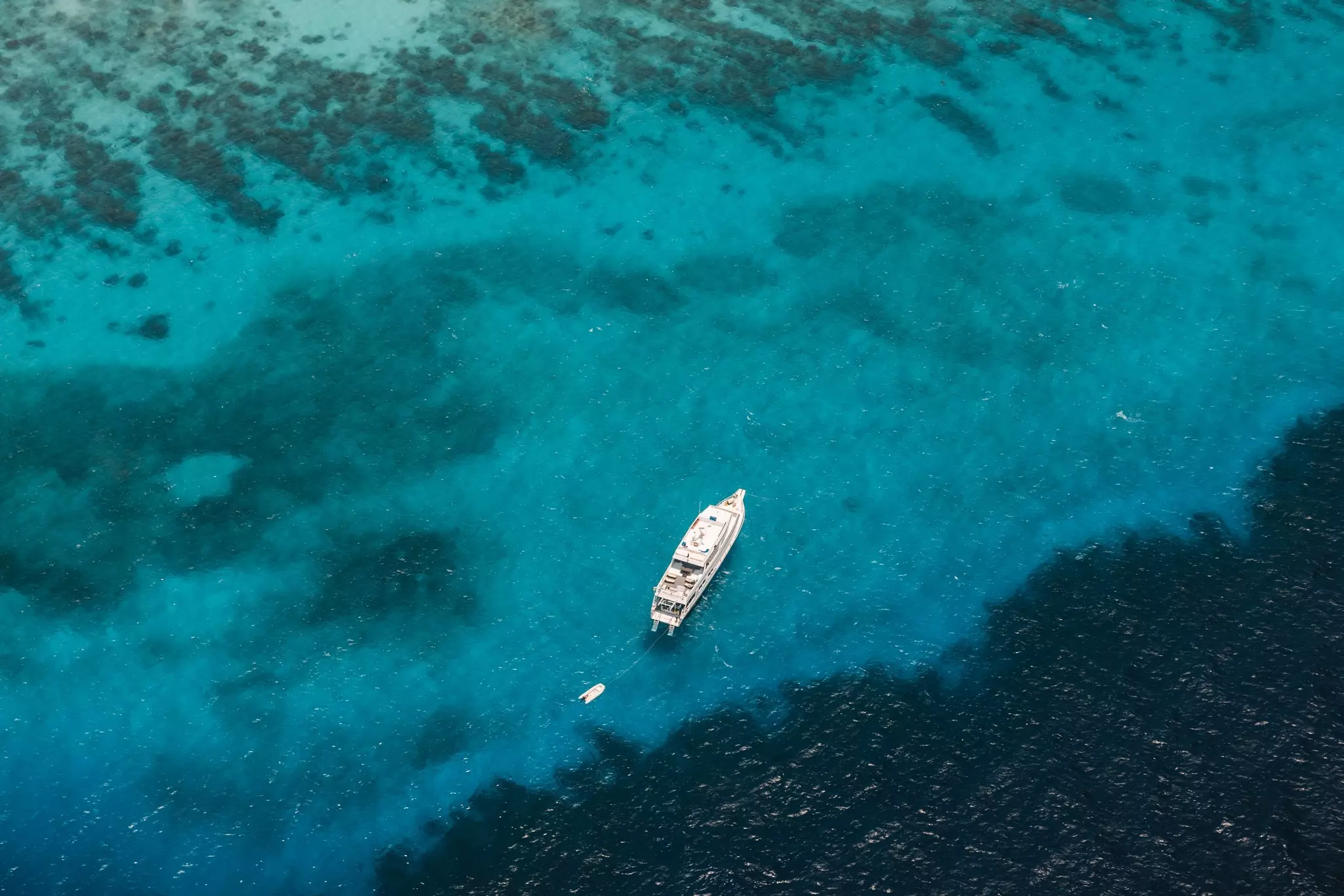 A large dive boat moored in the depths of the blue ocean adjacent to a dark barrier reef.