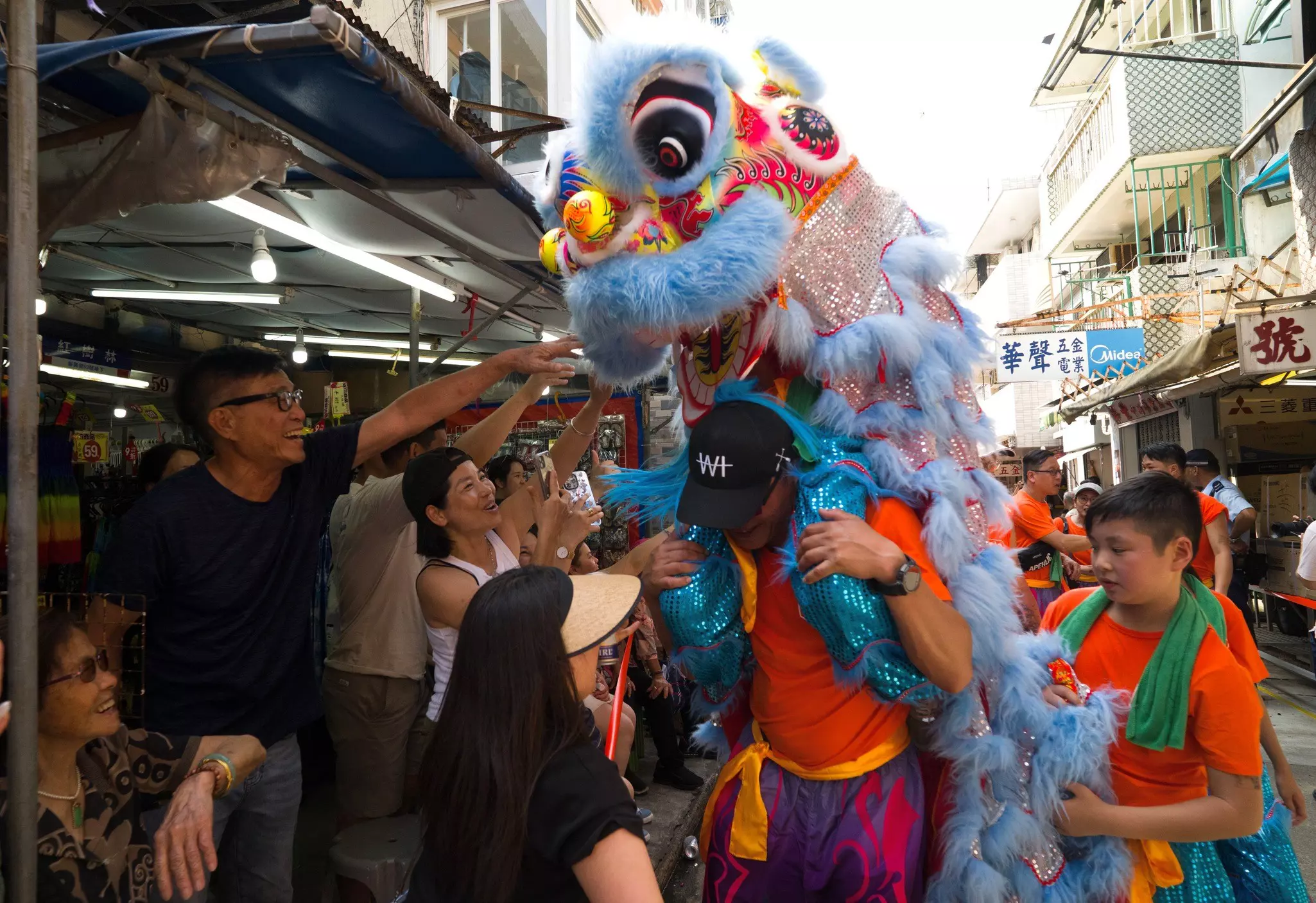 People gather around a man wearing a dragon costume during a parade in a narrow street in a town.
