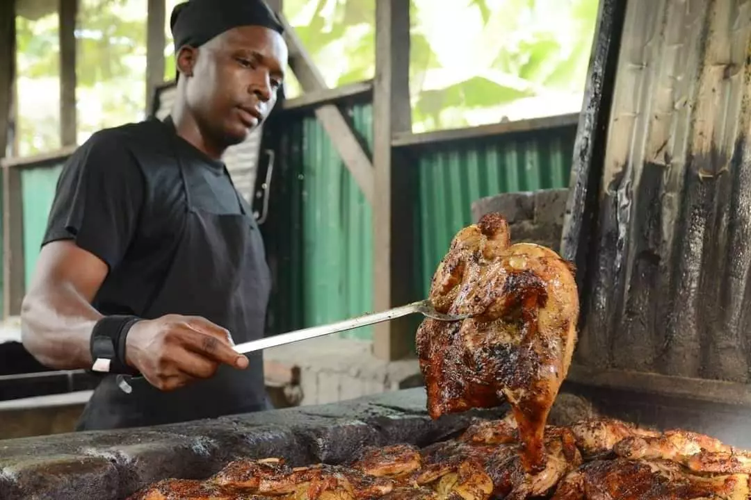 A chef spears a whole chicken cooking on a grill at a barbecue restaurant