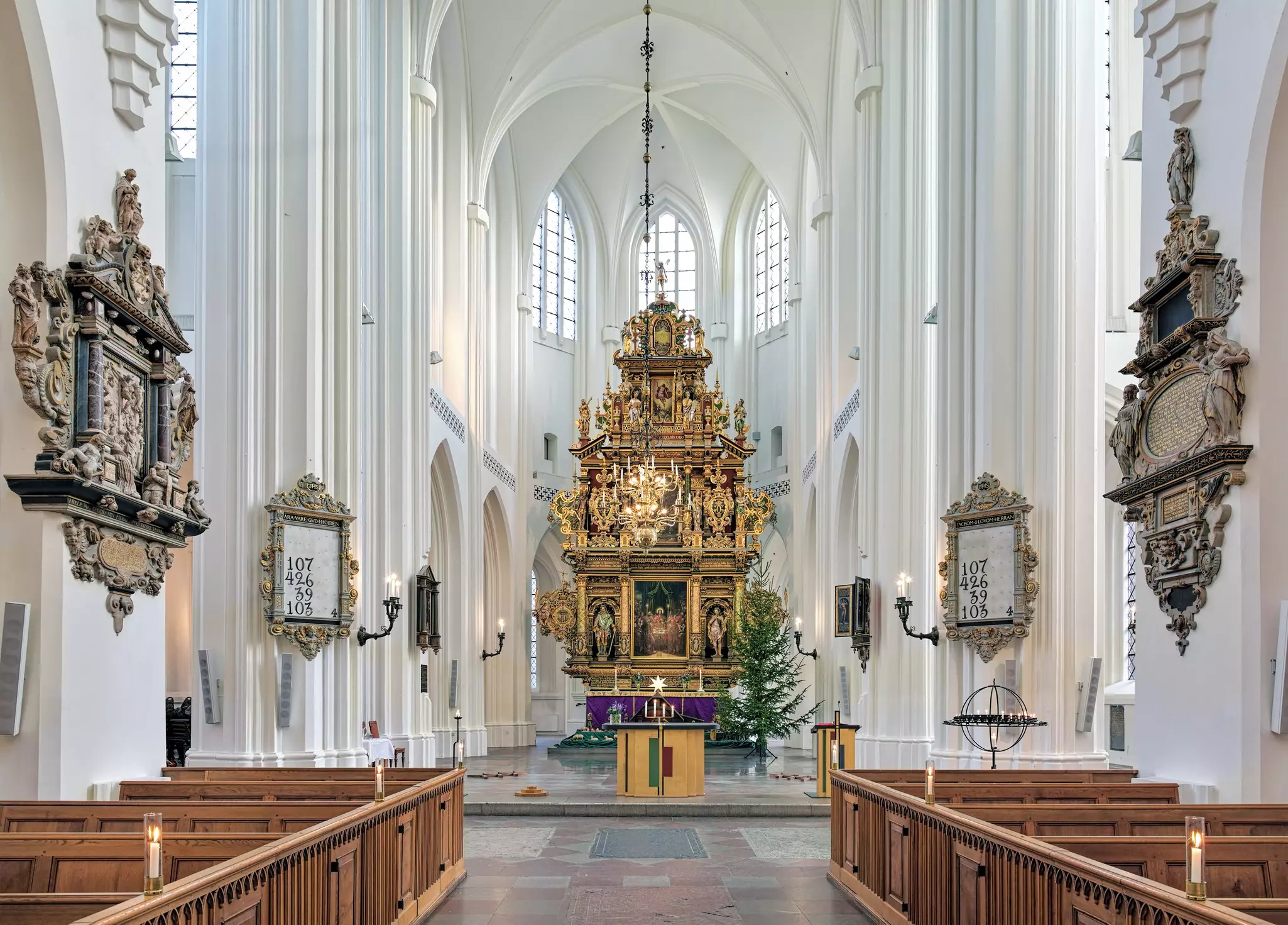 An elaborately carved altarpiece is seen in the nave of a medieval church in Malmö, Sweden, with white pillars and vaulted ceilings.