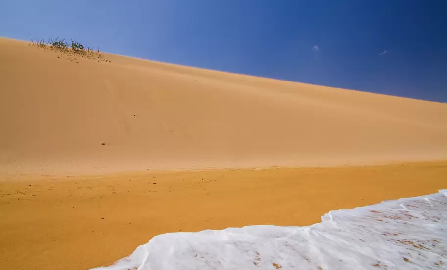 Tall golden sand dune sloping down to white surf on the Caribbean shore under a deep blue sky, La Guajira Peninsula, Colombia