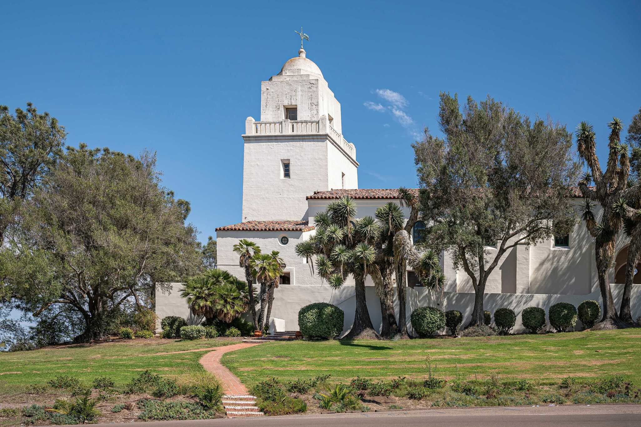 San Diego, California, USA - October 3, 2021: Tower of Junipero Serra Museum white building against blue sky on its hill and green foliage up front