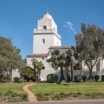 San Diego, California, USA - October 3, 2021: Tower of Junipero Serra Museum white building against blue sky on its hill and green foliage up front