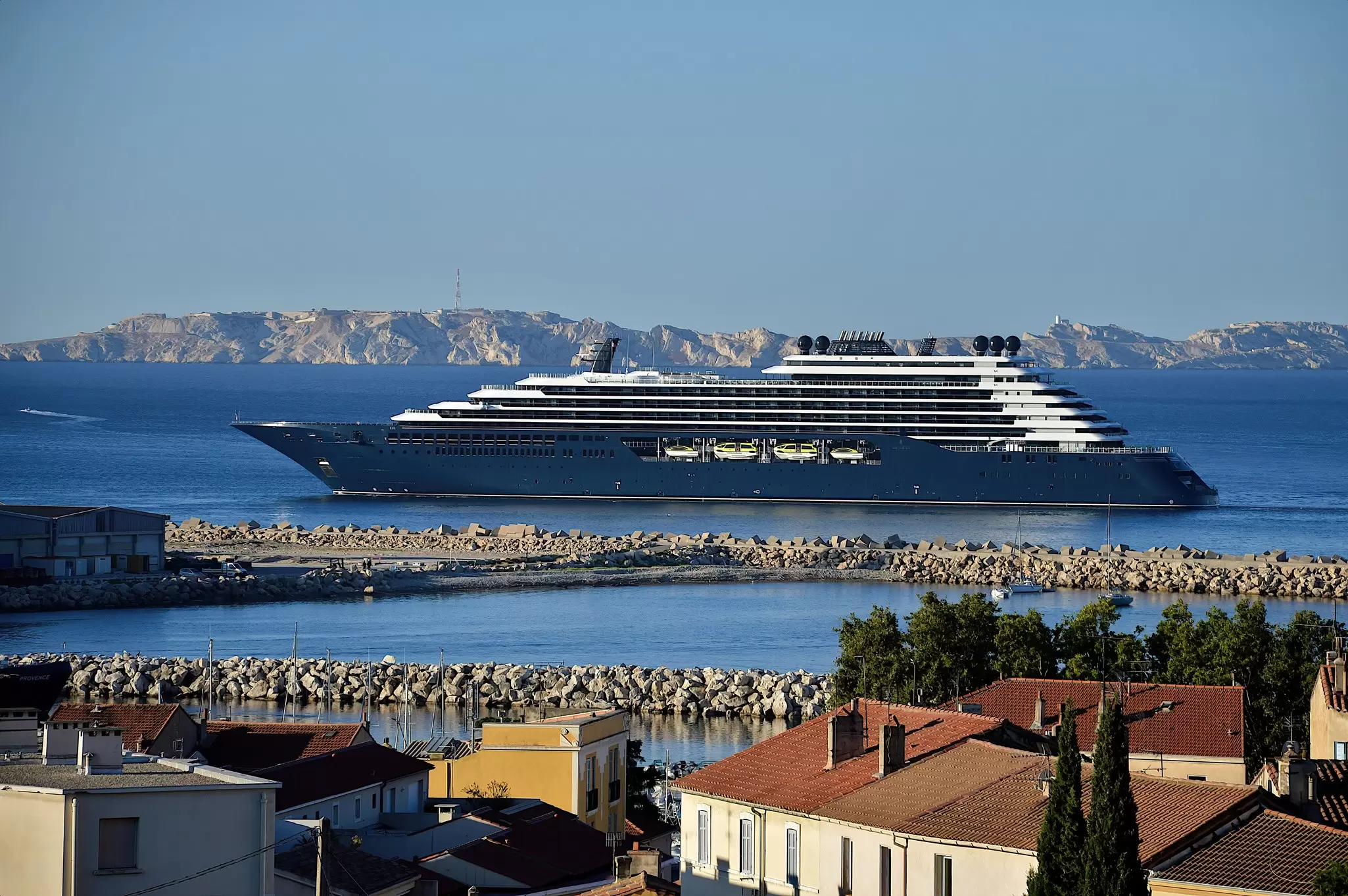 A large cruise ship sails past a breakwater as it nears a city port, Marseille, France