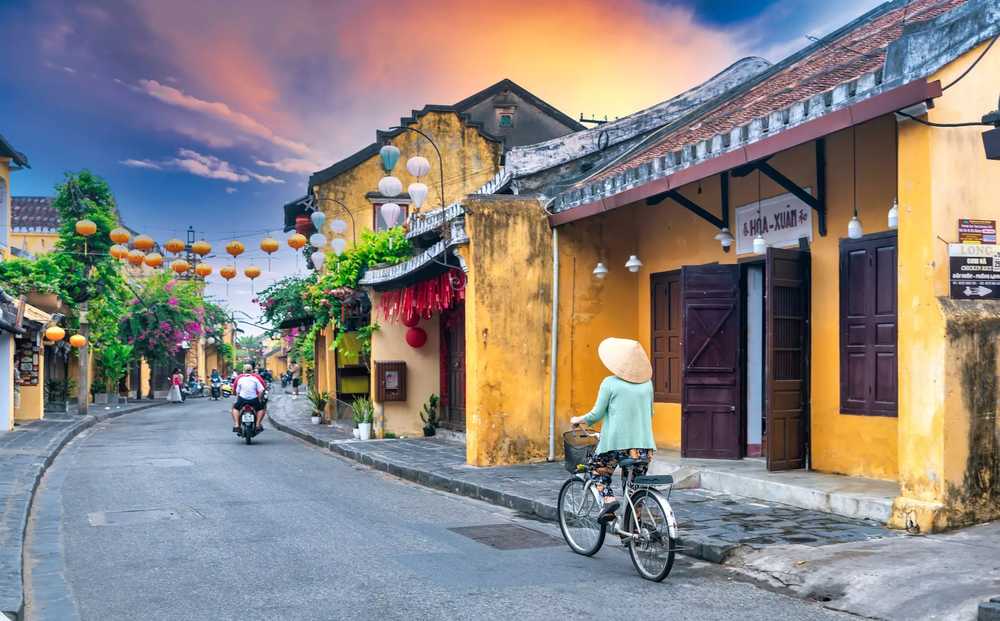 A woman cycles down the narrow lane of an old town in Hoi An, Vietnam