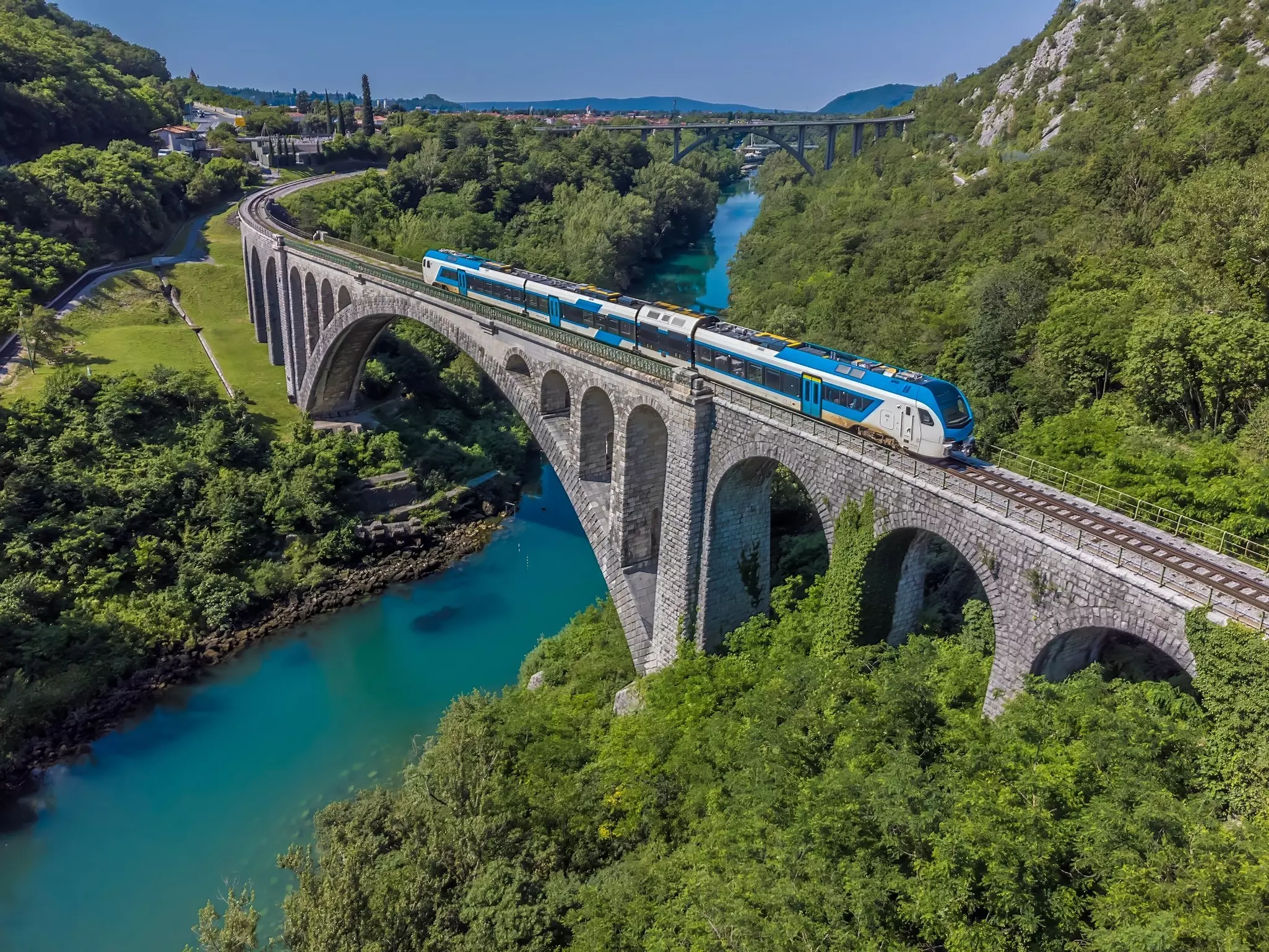An aerial view of a train crossing the stone railway bridge on the outskirts of the town of Solkan in Slovenia in summertime