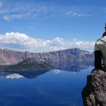 A lone young woman sitting on the rock in front of water in the Crater Lake National Park, Garfield Peak trail (OR, USA), License Type: media, Download Time: 2025-08-14T04:16:50.000Z, User: claramonitto, Editorial: false, purchase_order: 56530 - Guidebooks, job: Global Publishing-WIP, client: Washington, Oregon & Pacific Northwest 10, other: Clara Monitto