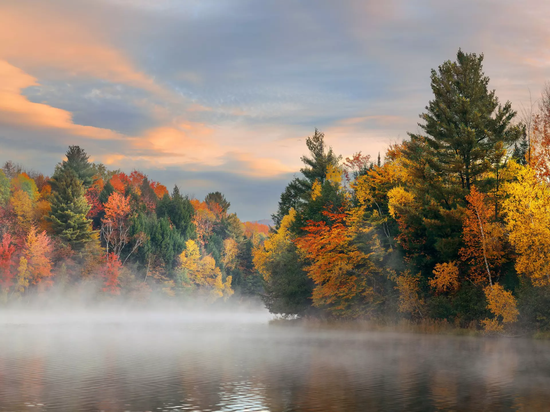A foggy view of a lake with colorful trees in fall.