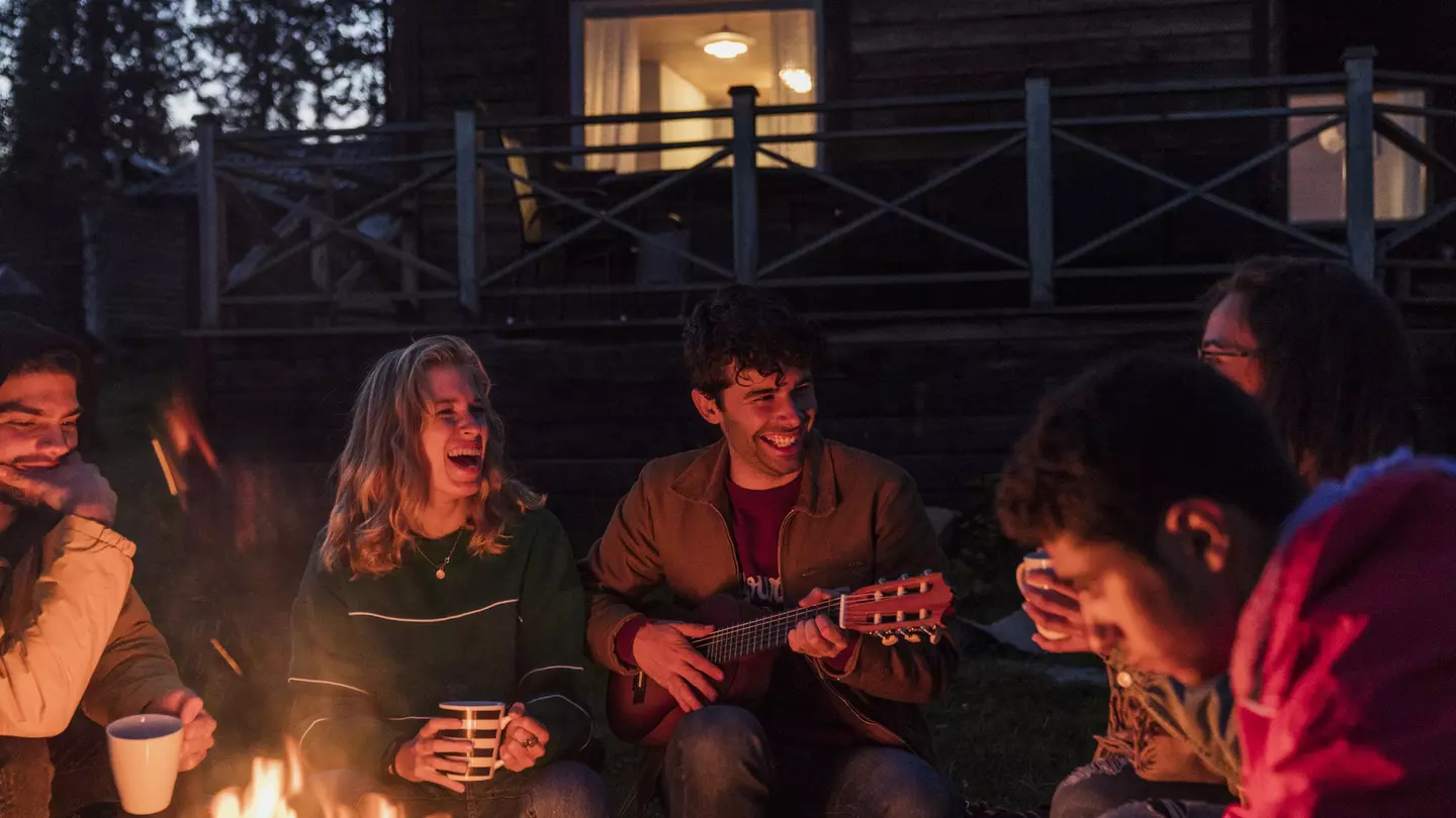 Group of friends sitting at a campfire, talking and playing guitar