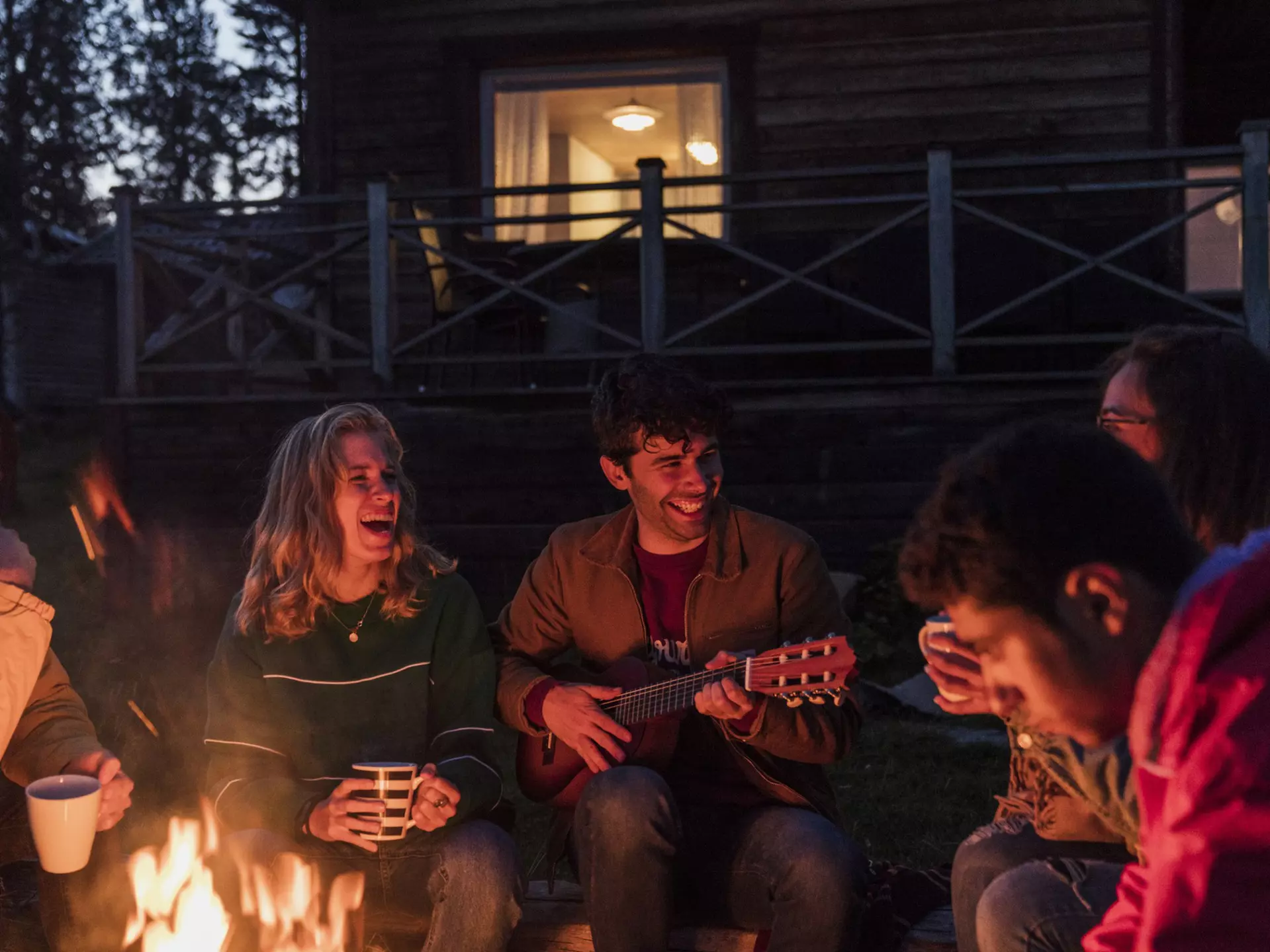 Group of friends sitting at a campfire, talking and playing guitar