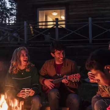 Group of friends sitting at a campfire, talking and playing guitar