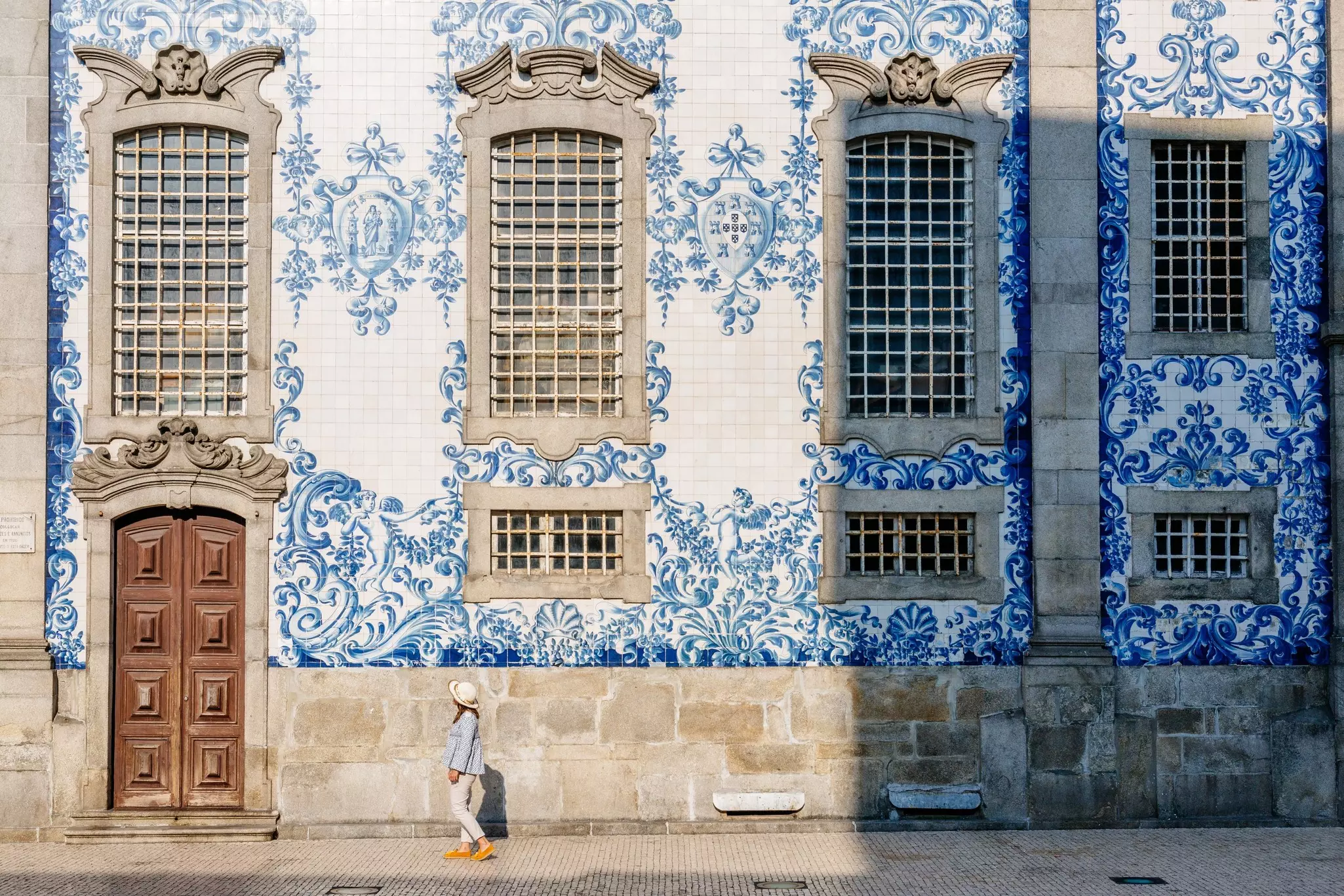 A woman walks past the tiled facade of a church, with blue and white tiles forming repeated patterns.