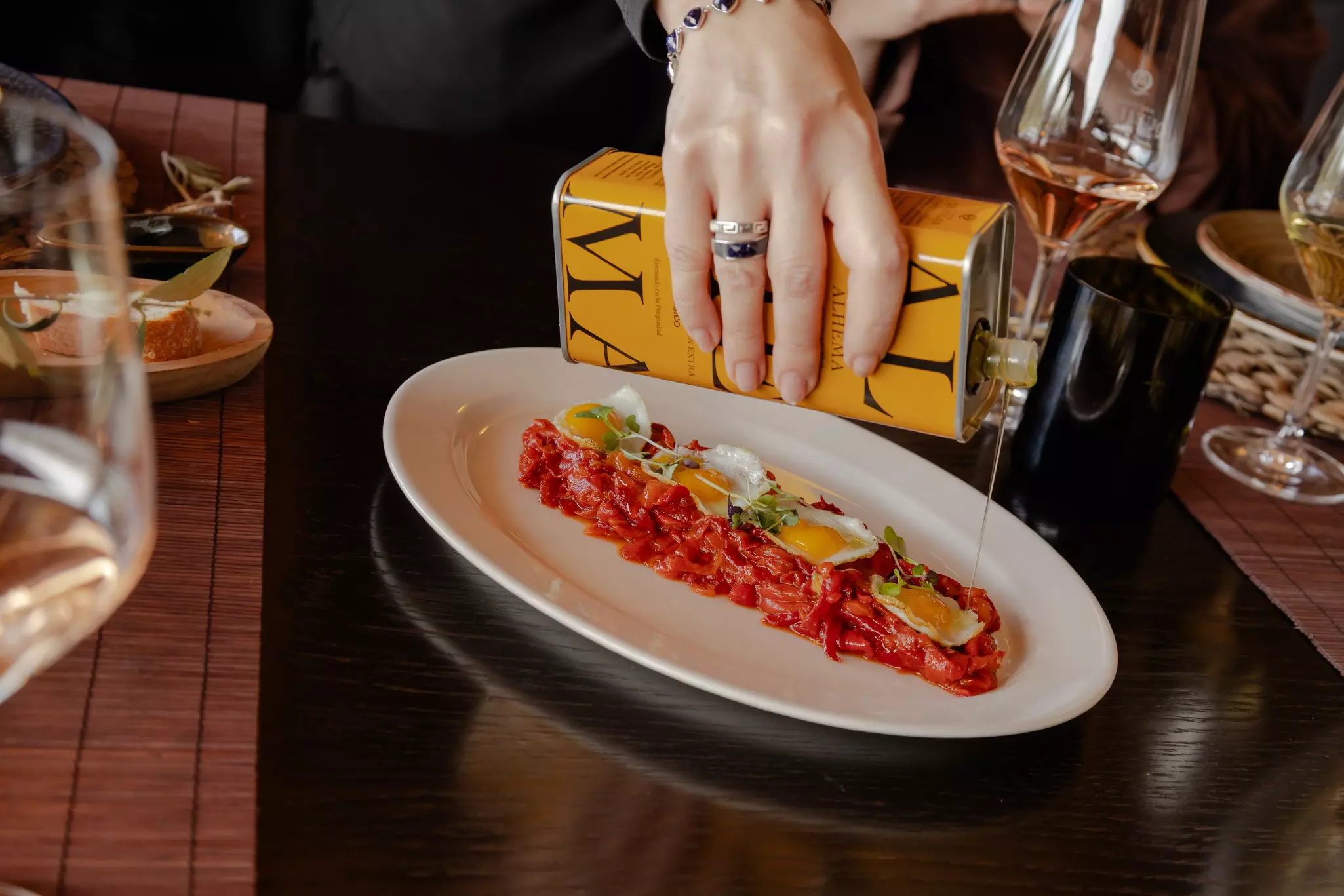 A hand pours oil from a can over food on a long plate.