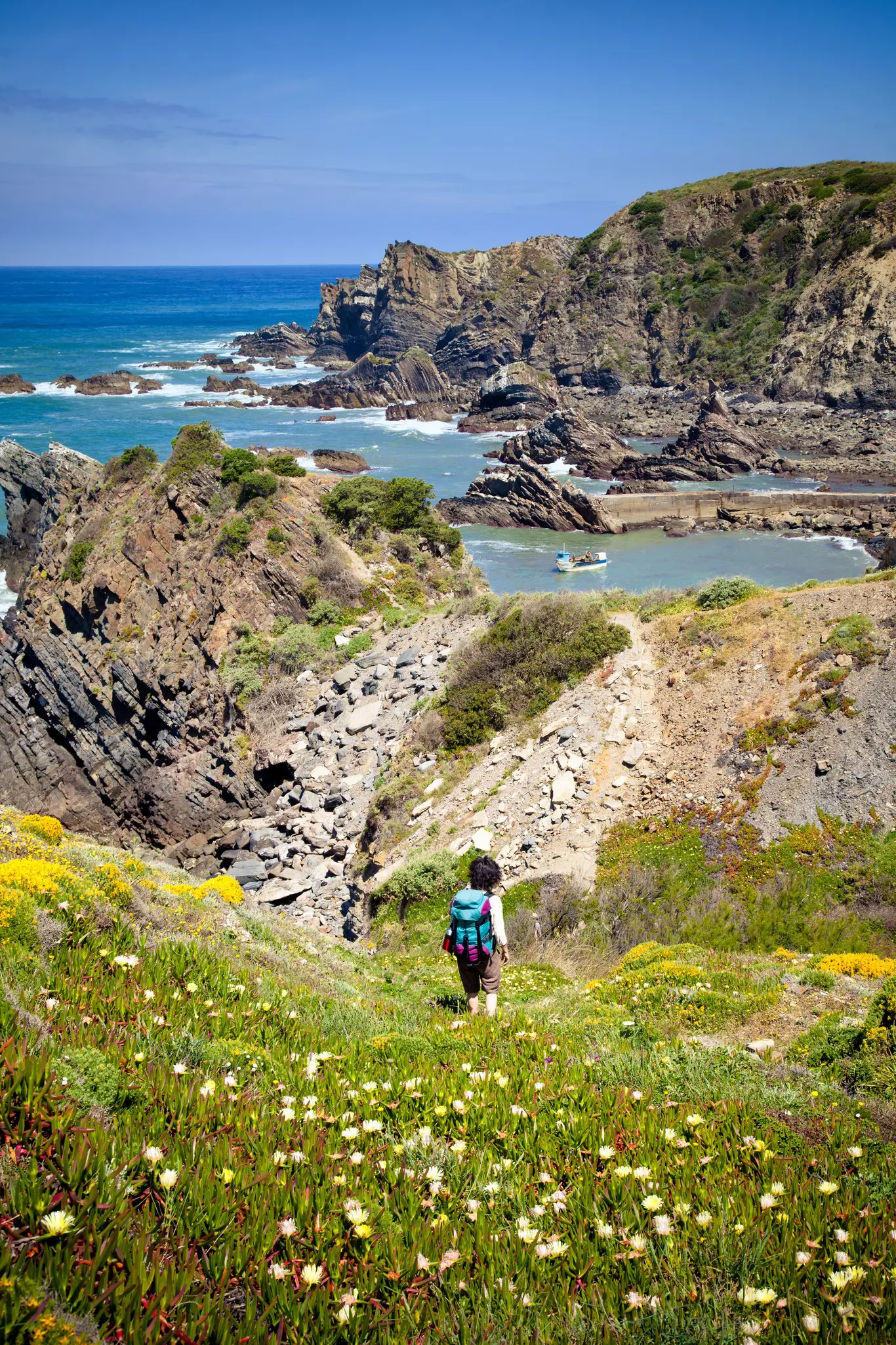 Person making their way down a grassy hill towrd a rocky incline near an ocean