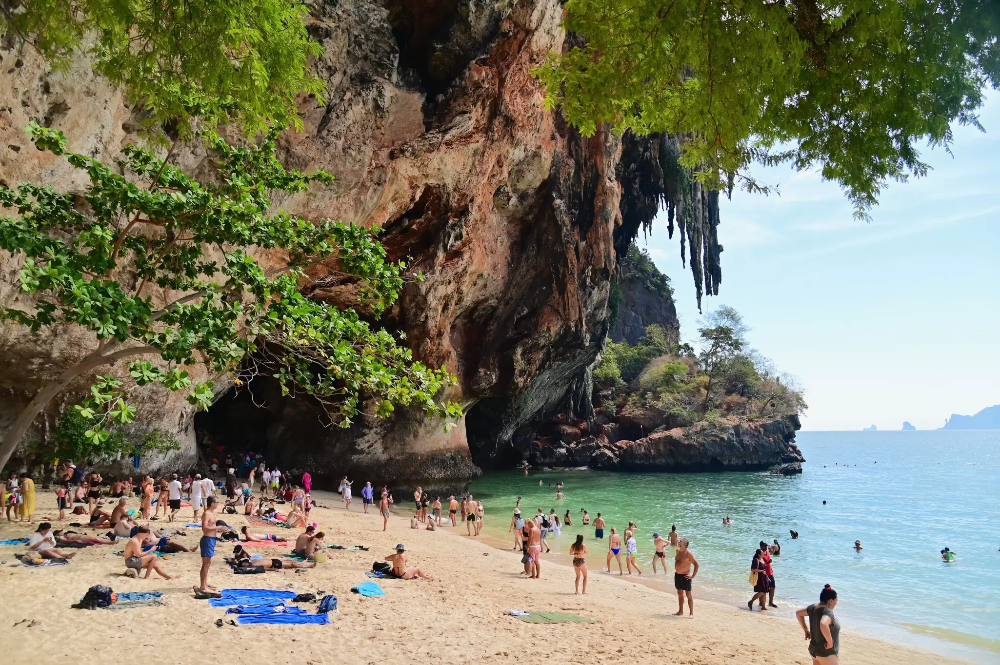 Tourists relaxing at Phra Nang beach near Hat Railay beach in Thailand, surrounded by rock formations.