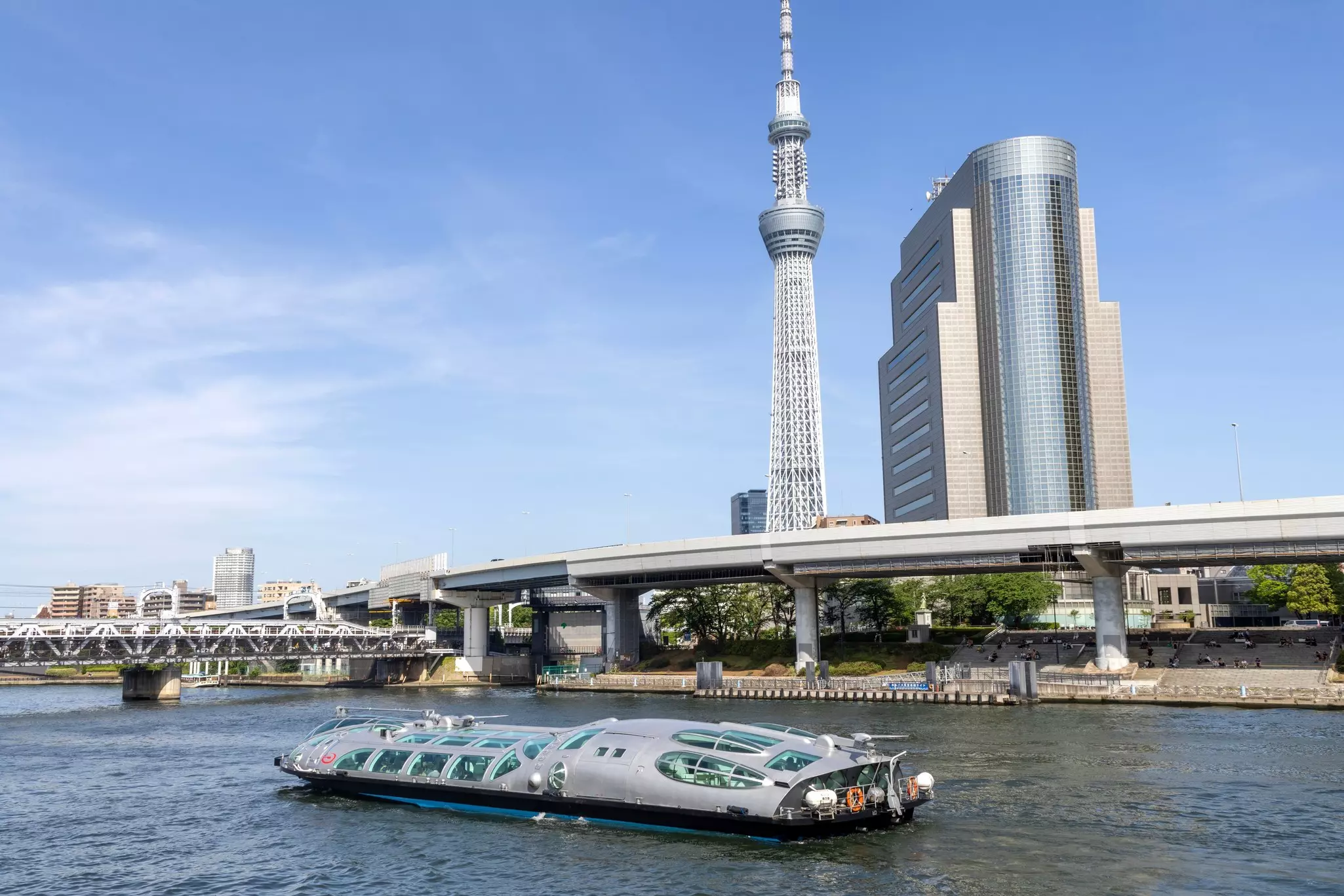 A ferry plies a river in a city. Two tall towers are seen on shore.
