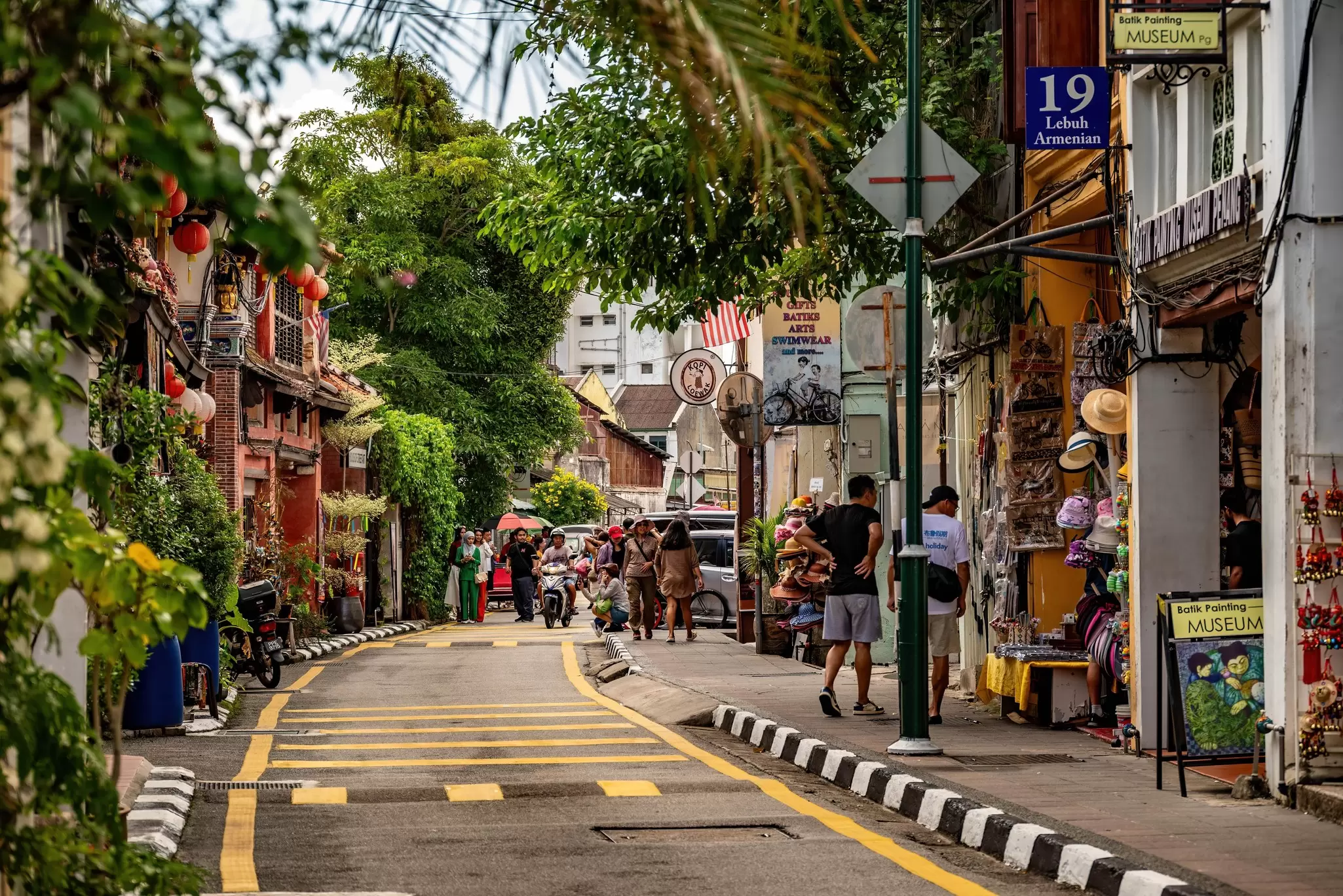 People walk down a city street lined with palm trees and shops.