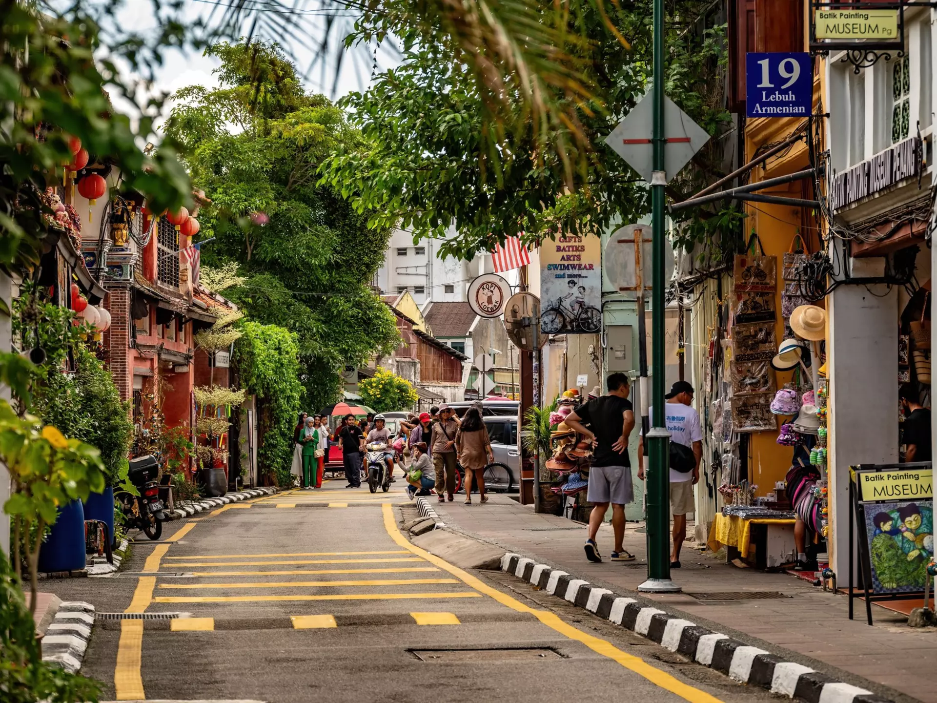 People walk down a city street lined with palm trees and shops.