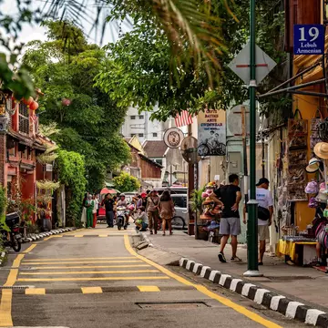 People walk down a city street lined with palm trees and shops.
