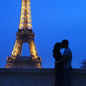 A couple embracing in front of the Eiffel Tower at night.