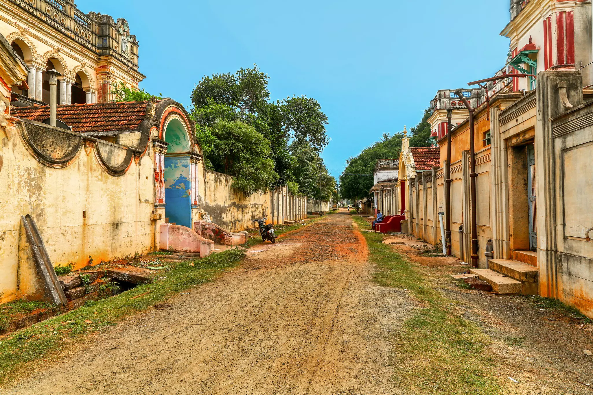 An unpaved street in a village leads past the walls of large historic houses.