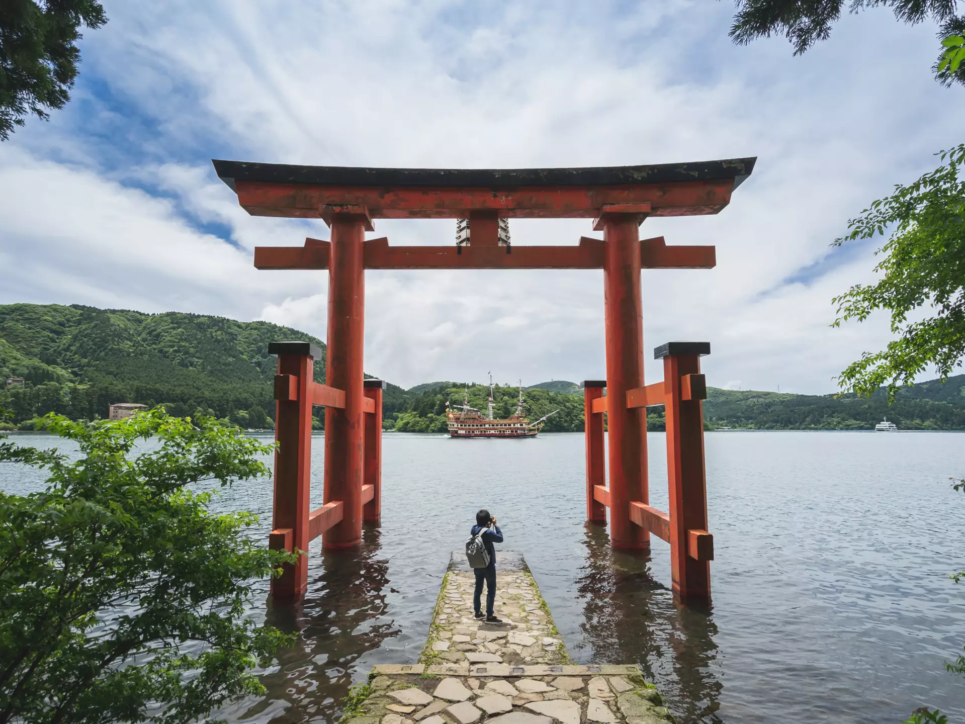 A person under a red gate by a lake with a boat on the water.