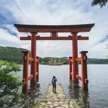 A person under a red gate by a lake with a boat on the water.