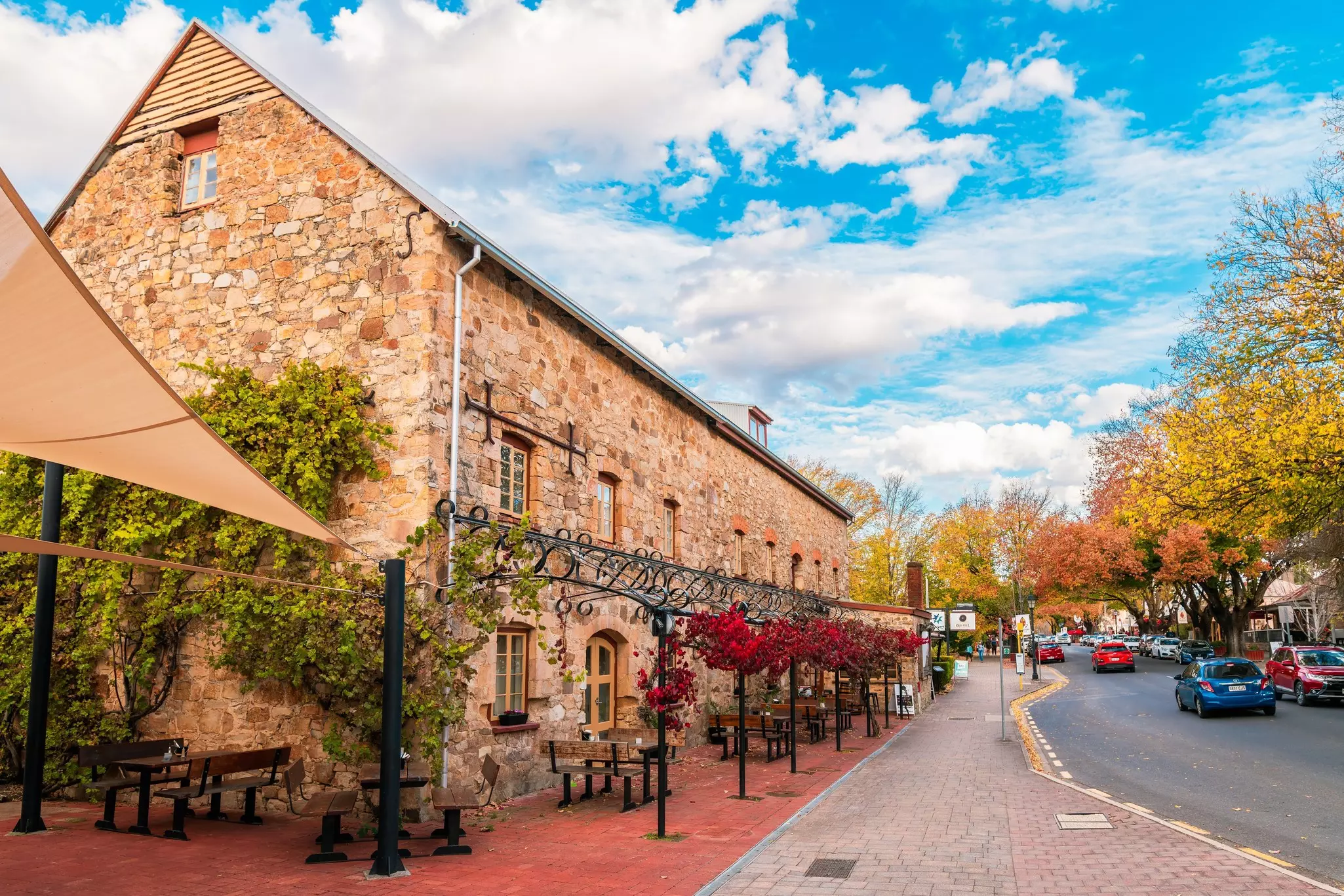 An old stone building on a street lined with trees changing to fall colors