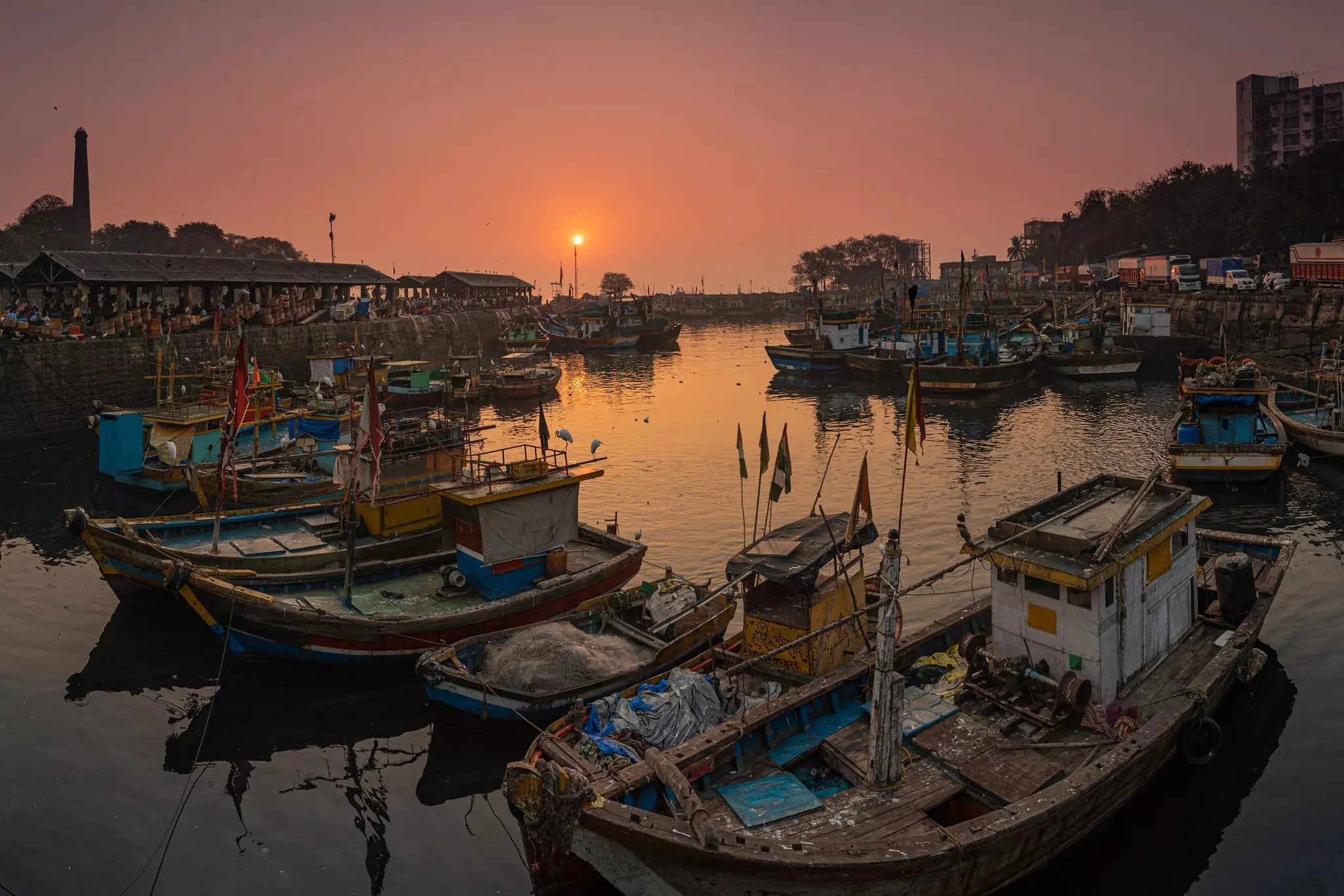 Many wooden fishing boats docked together in a small harbor at sunset.