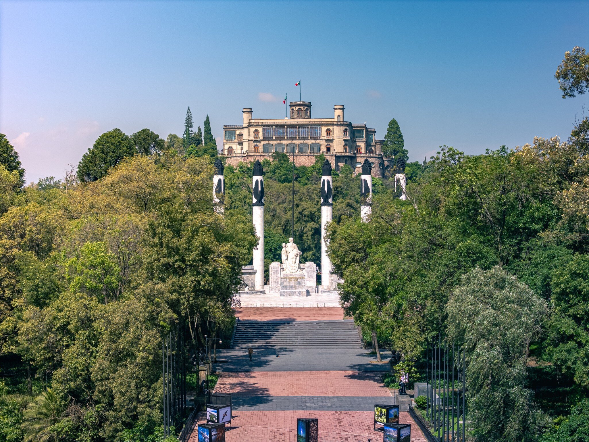 Aerial view over Bosque de Chapultepec, with the Castillo de Chapultepec and Monumento a los Niños Héroes in the background, on a sunny day in Mexico City.
