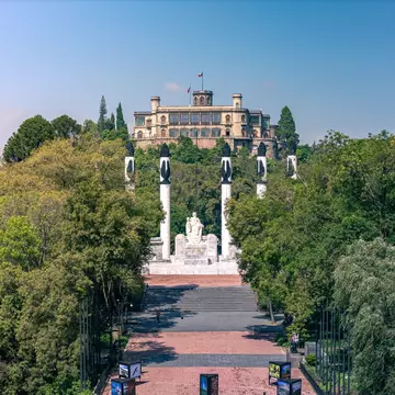 Aerial view over Bosque de Chapultepec, with the Castillo de Chapultepec and Monumento a los Niños Héroes in the background, on a sunny day in Mexico City.